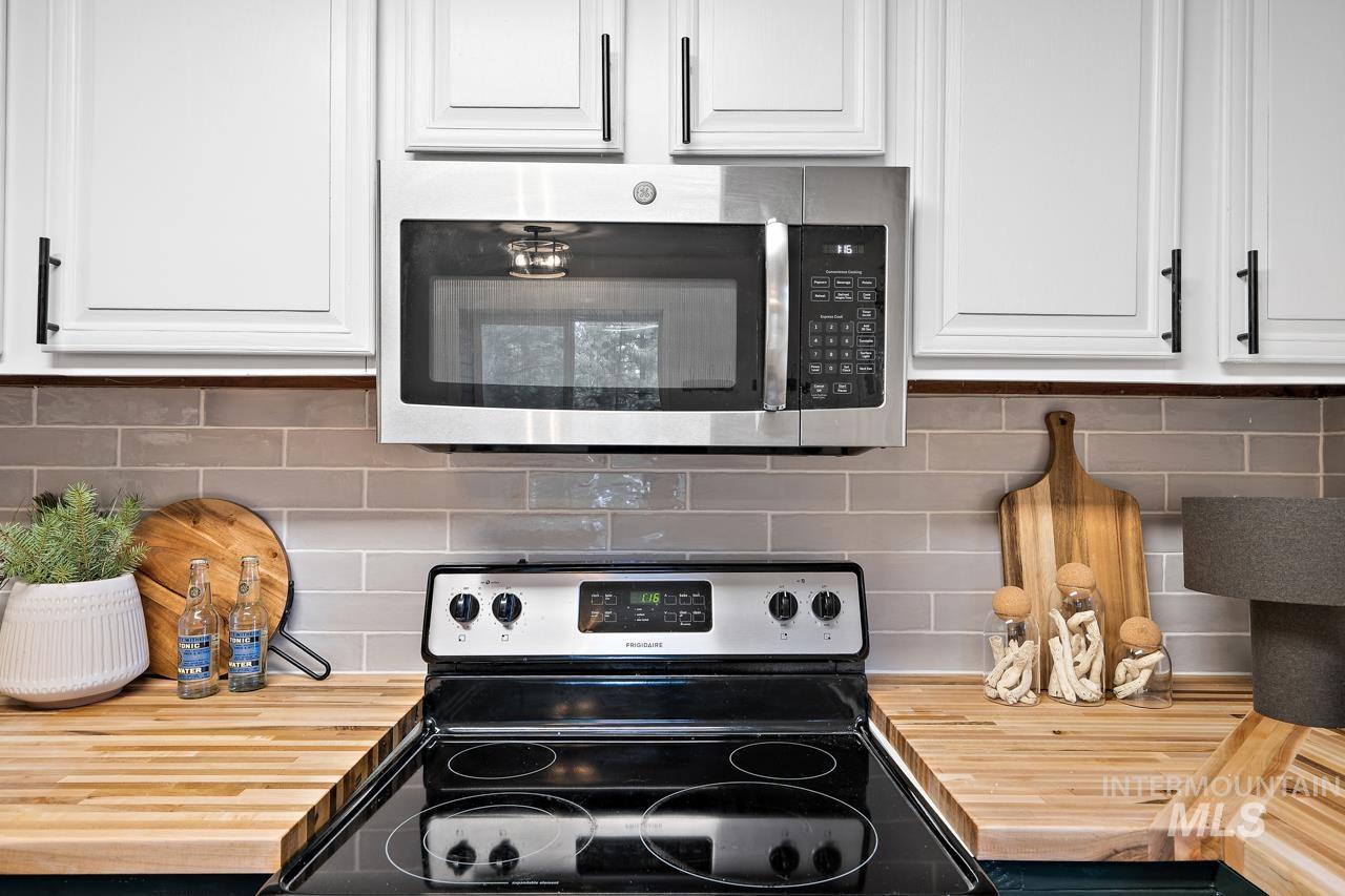 Kitchen featuring wooden counters, stainless steel appliances, tasteful backsplash, and white cabinetry