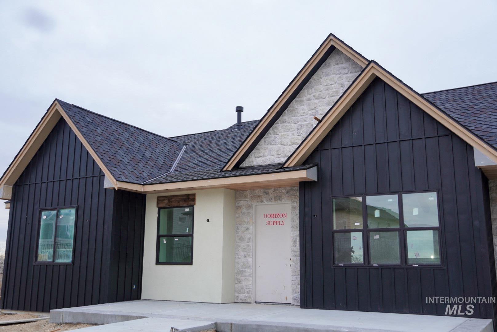 View of front of home with stone siding, a shingled roof, and board and batten siding