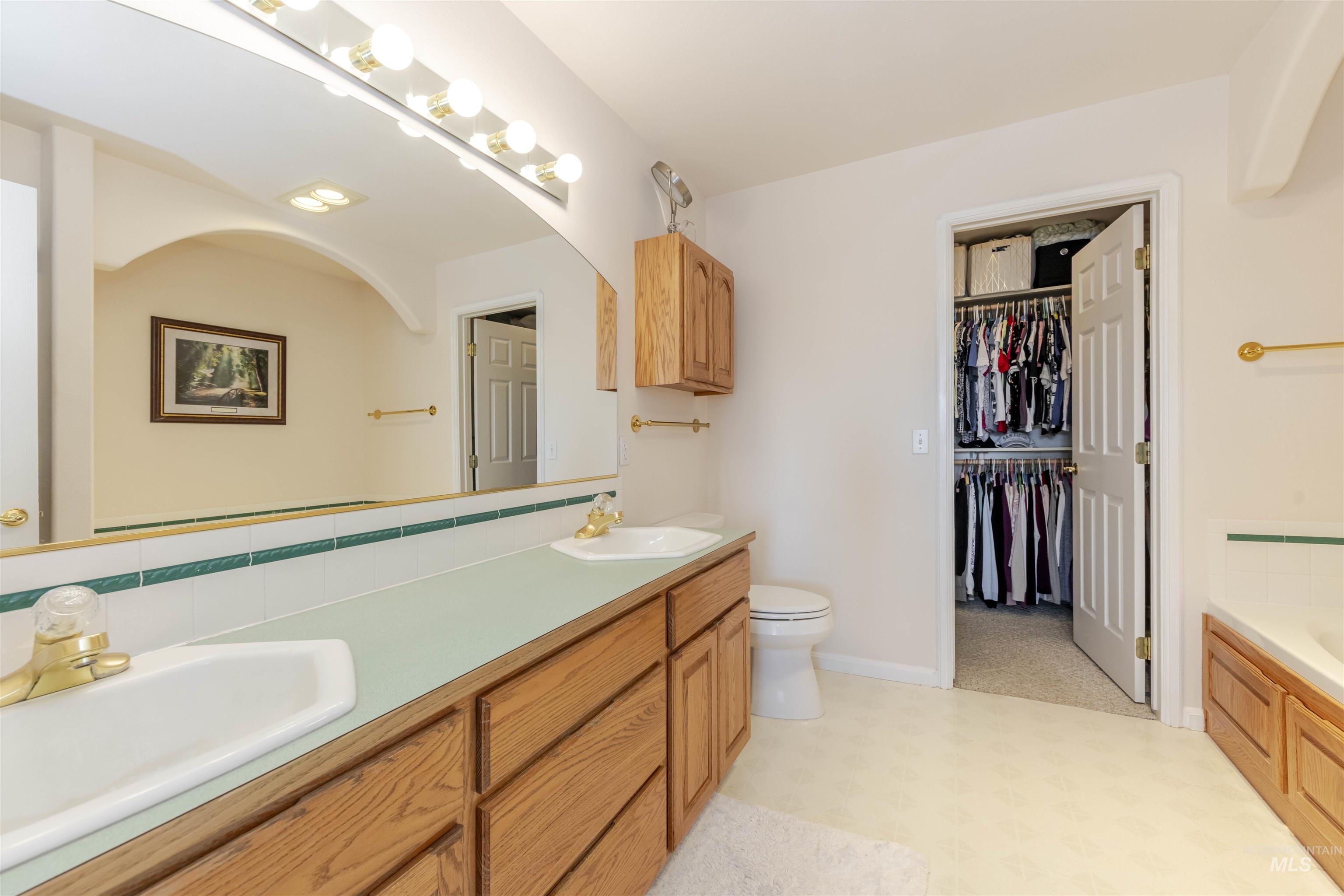 Full bath featuring double vanity, a tub to relax in, light flooring, decorative backsplash, and a spacious closet