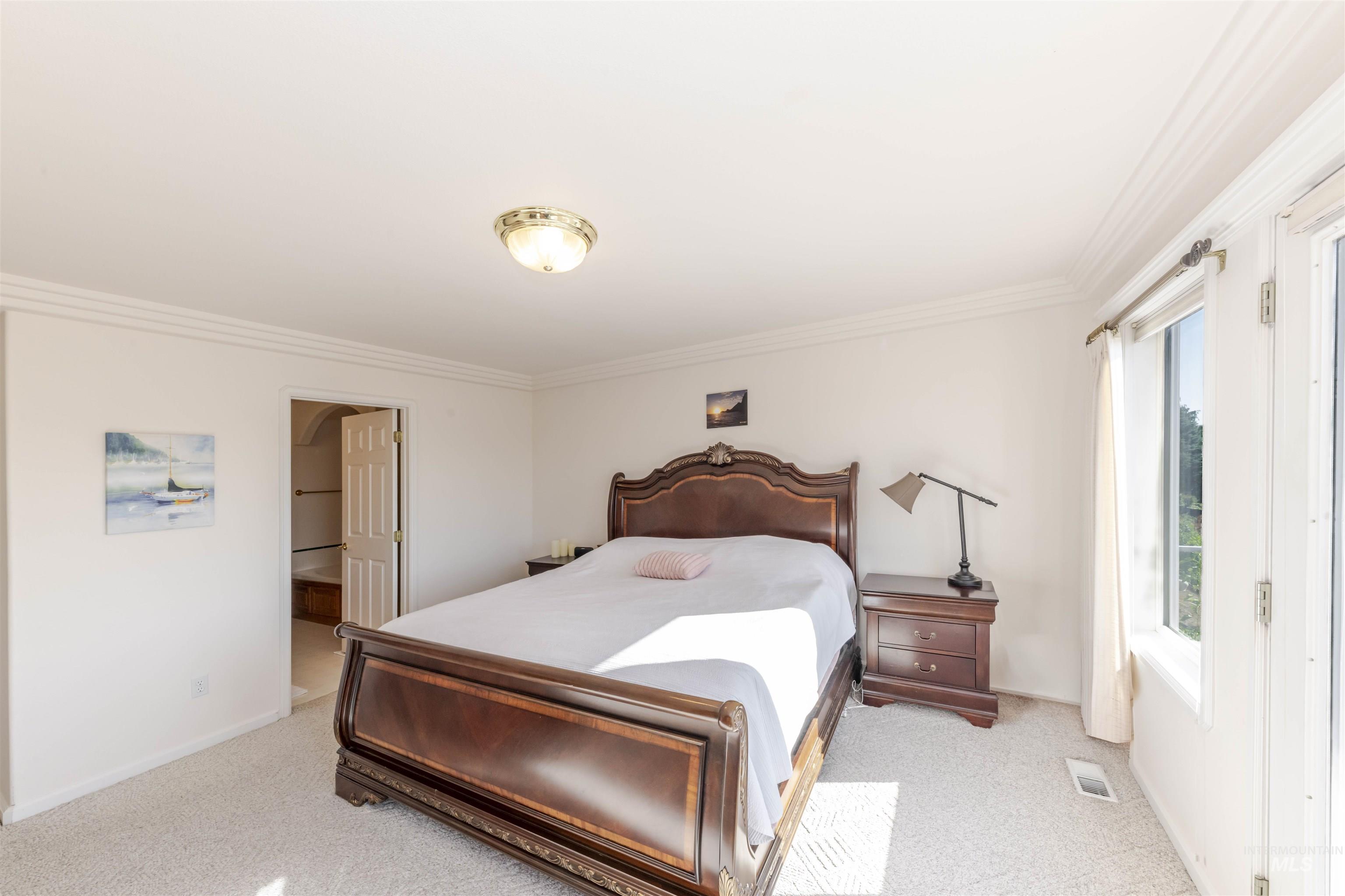 Bedroom with crown molding, light colored carpet, and connected bathroom