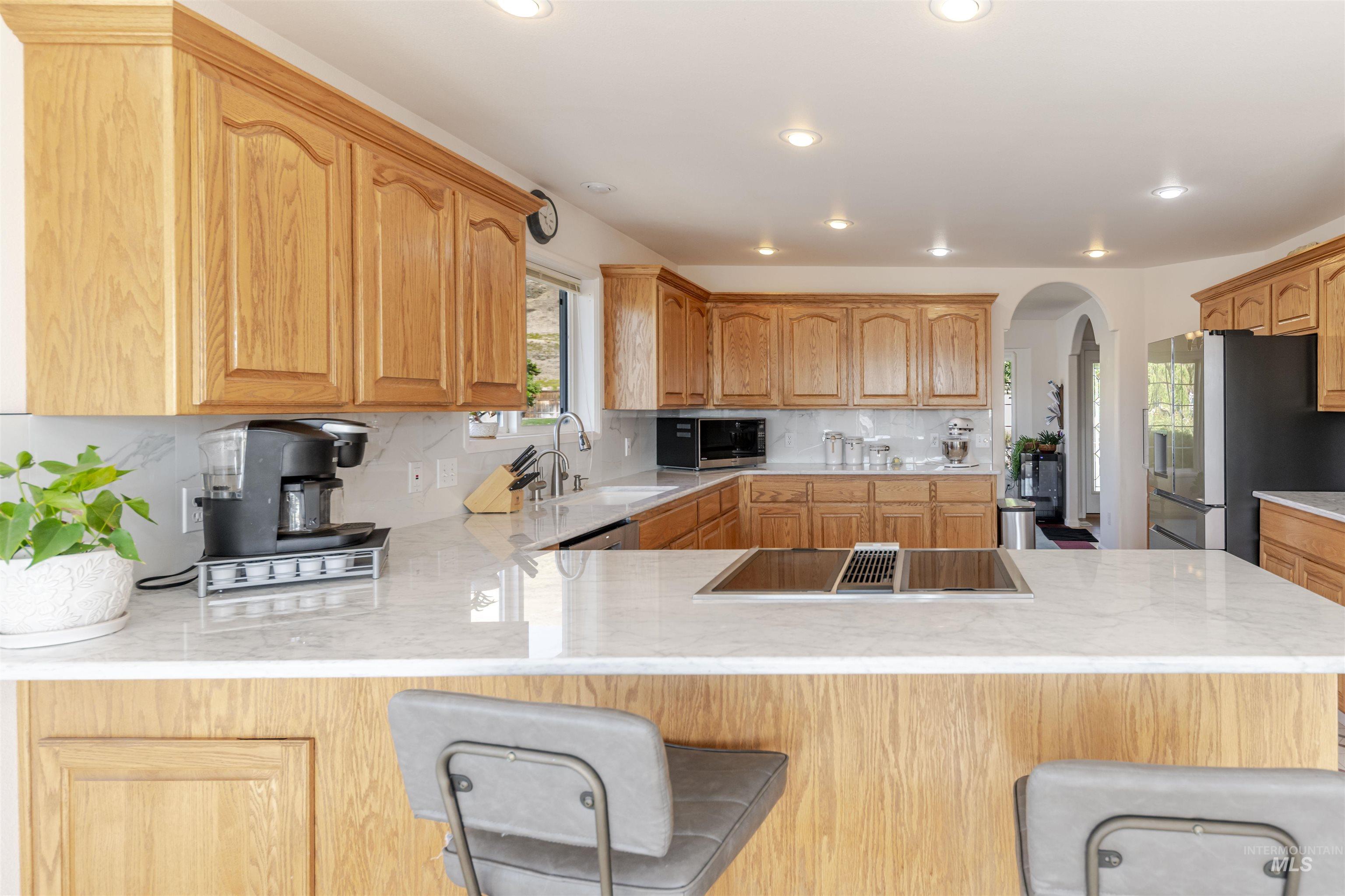 Kitchen featuring a breakfast bar, arched walkways, stainless steel appliances, backsplash, and light stone countertops