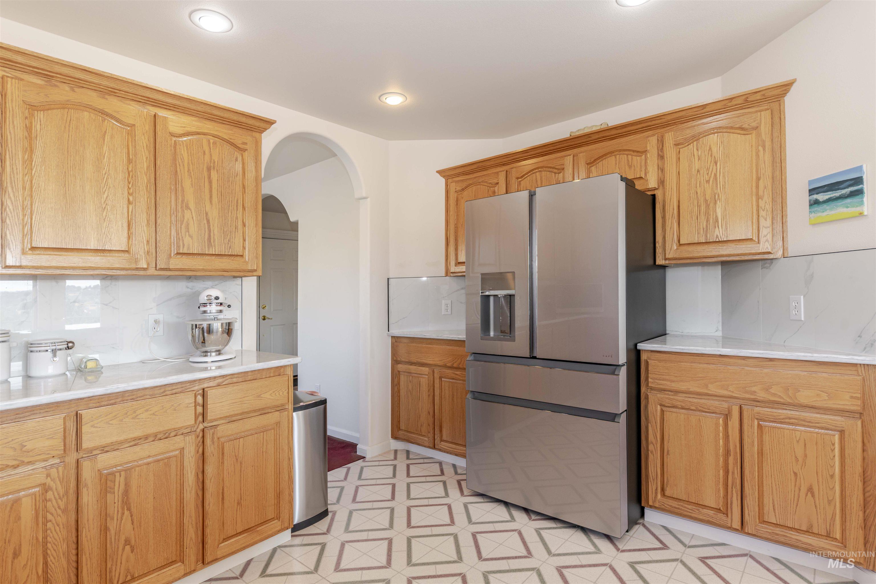 Kitchen with stainless steel fridge with ice dispenser, decorative backsplash, arched walkways, and light flooring