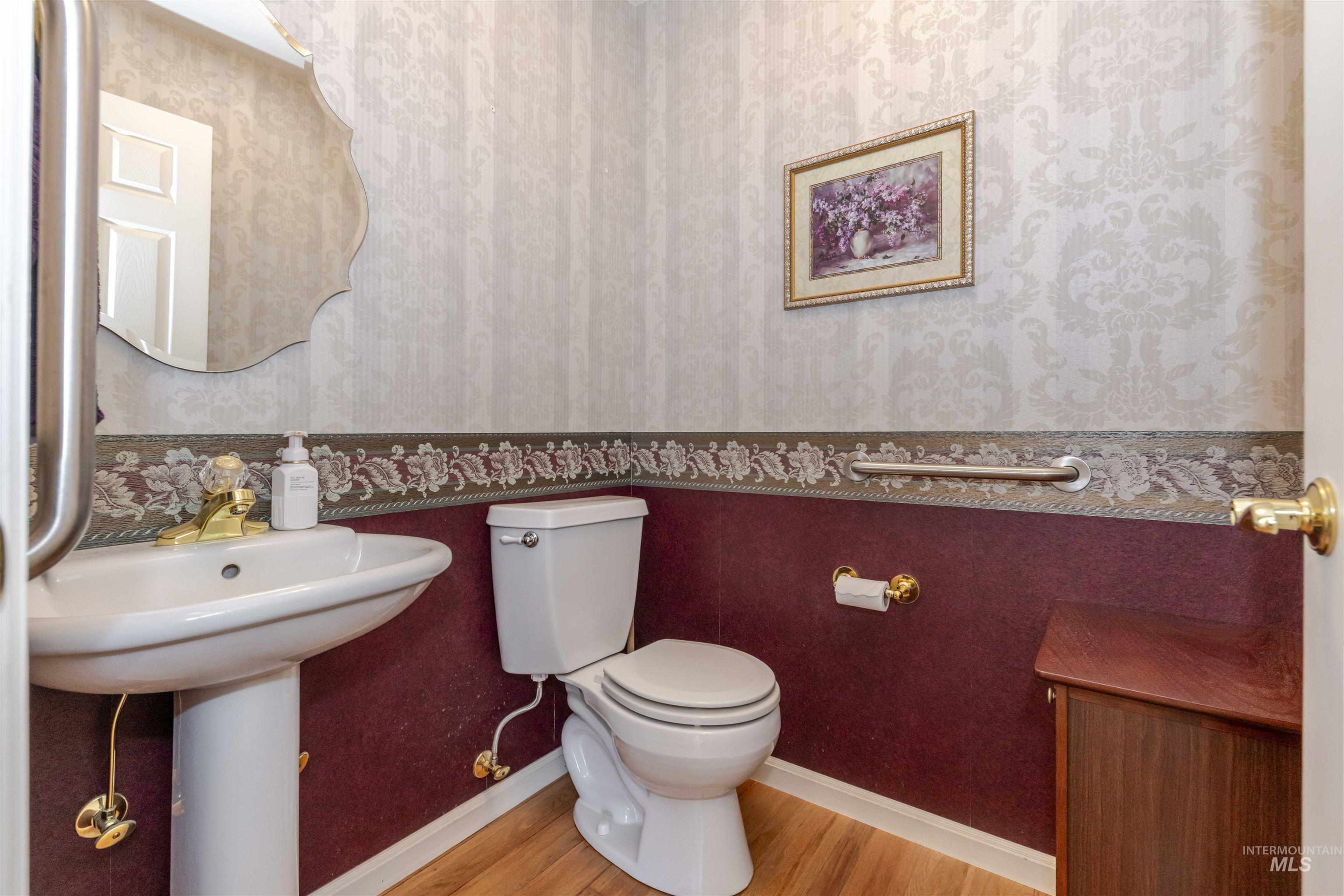 Half bath featuring wallpapered walls and wood finished floors