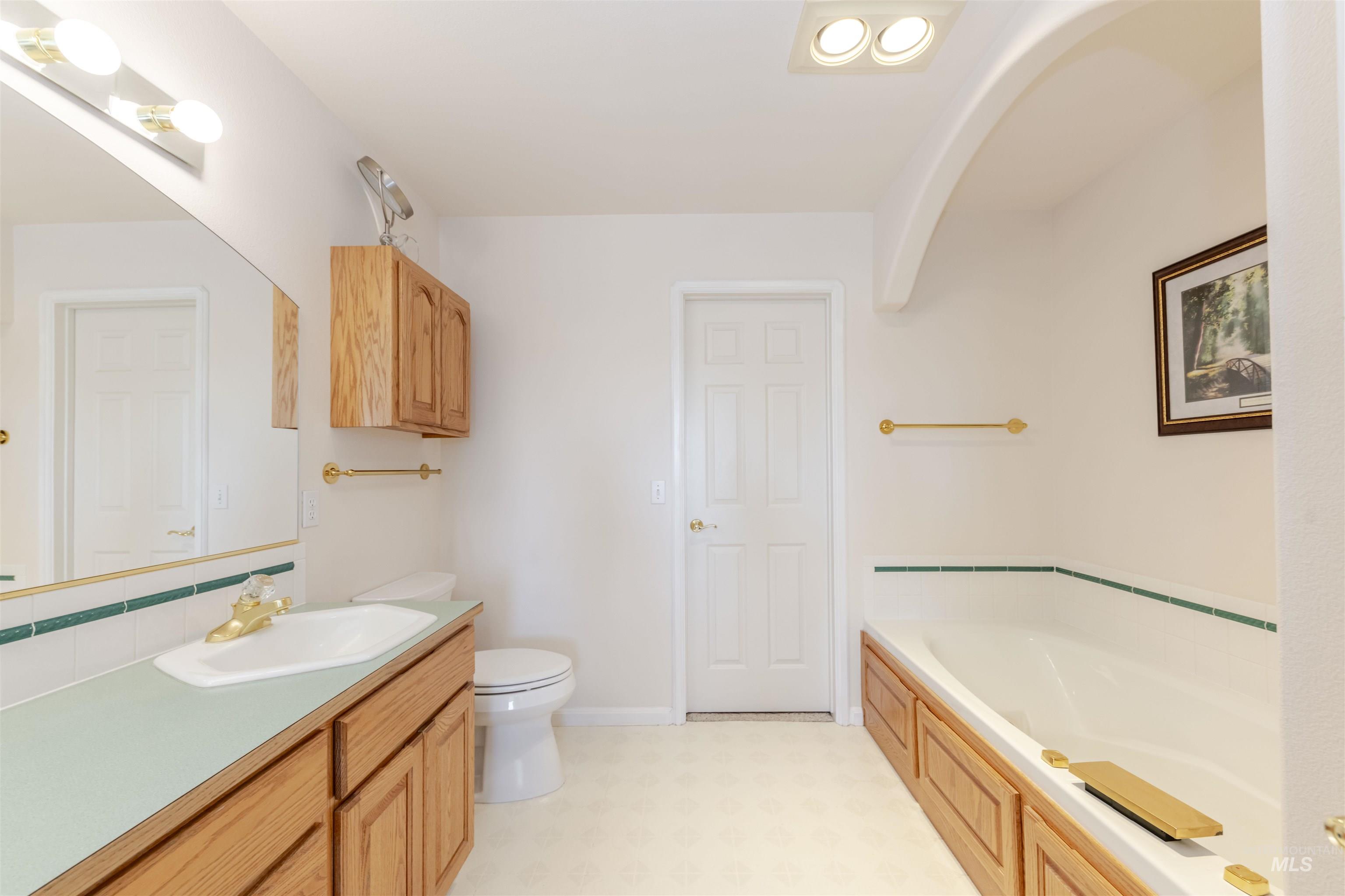 Full bathroom featuring a garden tub, vanity, light floors, and decorative backsplash