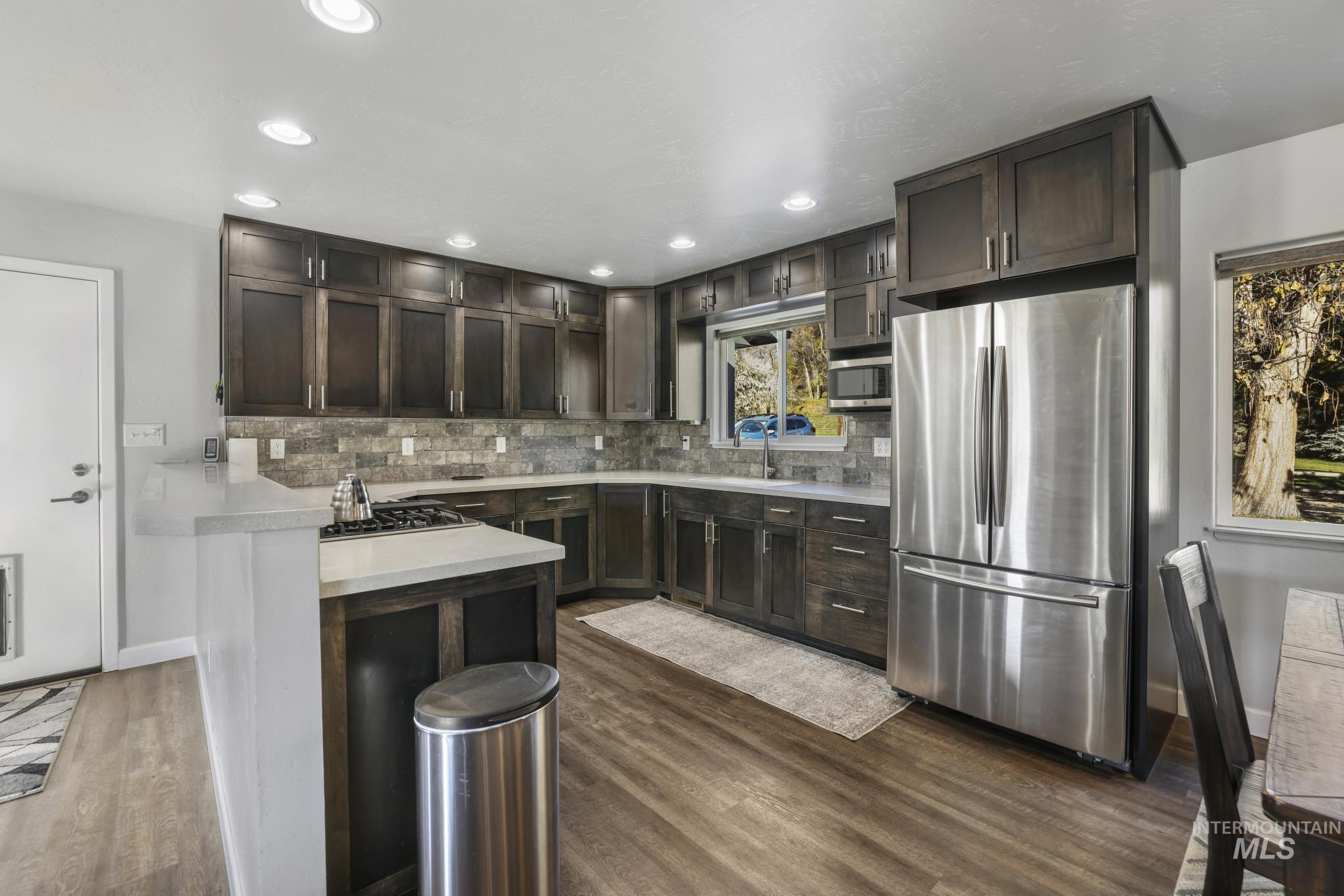 Kitchen featuring light countertops, stainless steel appliances, dark brown cabinets, tasteful backsplash, and a peninsula