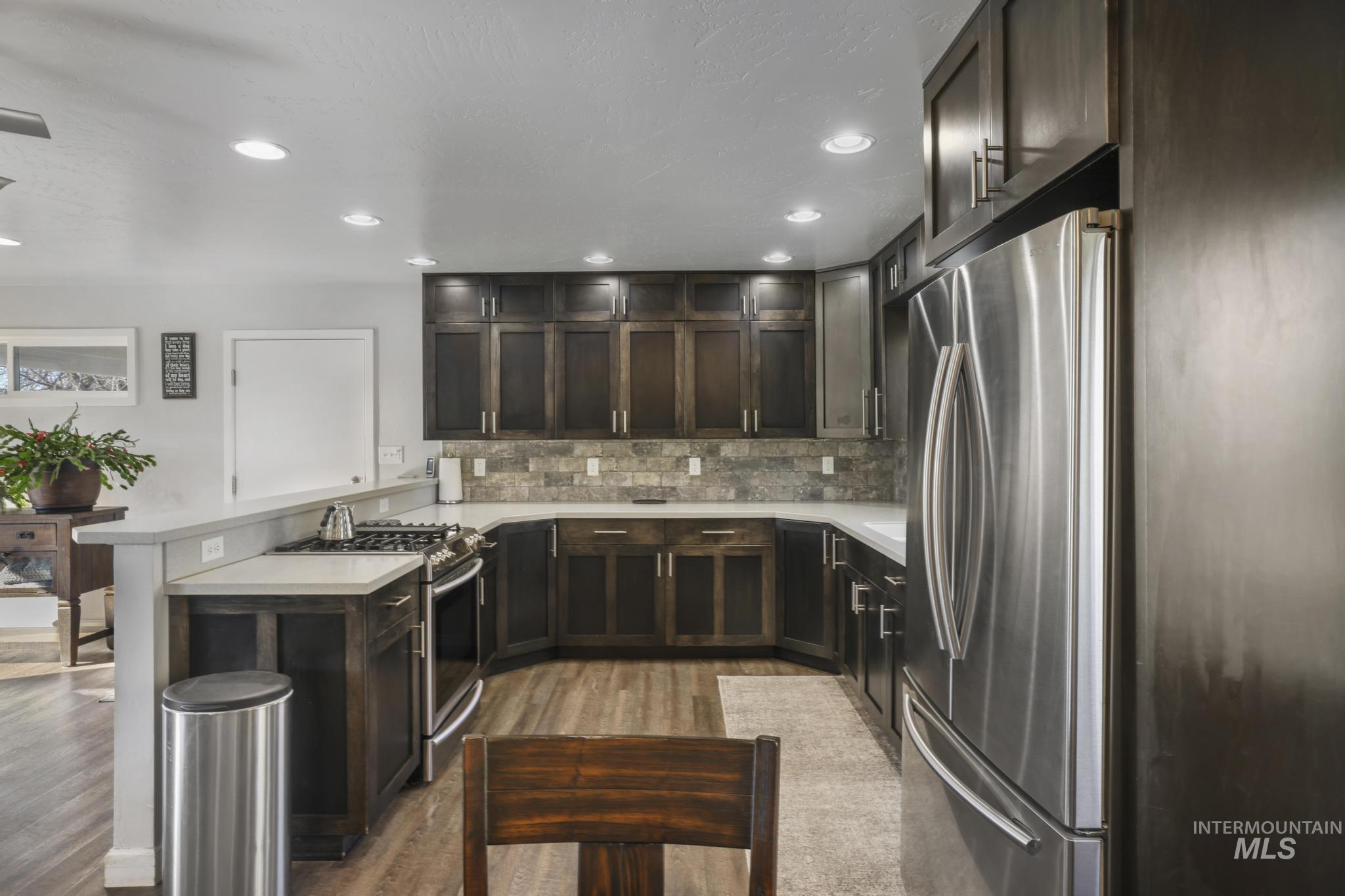Kitchen with a peninsula, stainless steel appliances, dark brown cabinets, backsplash, and recessed lighting