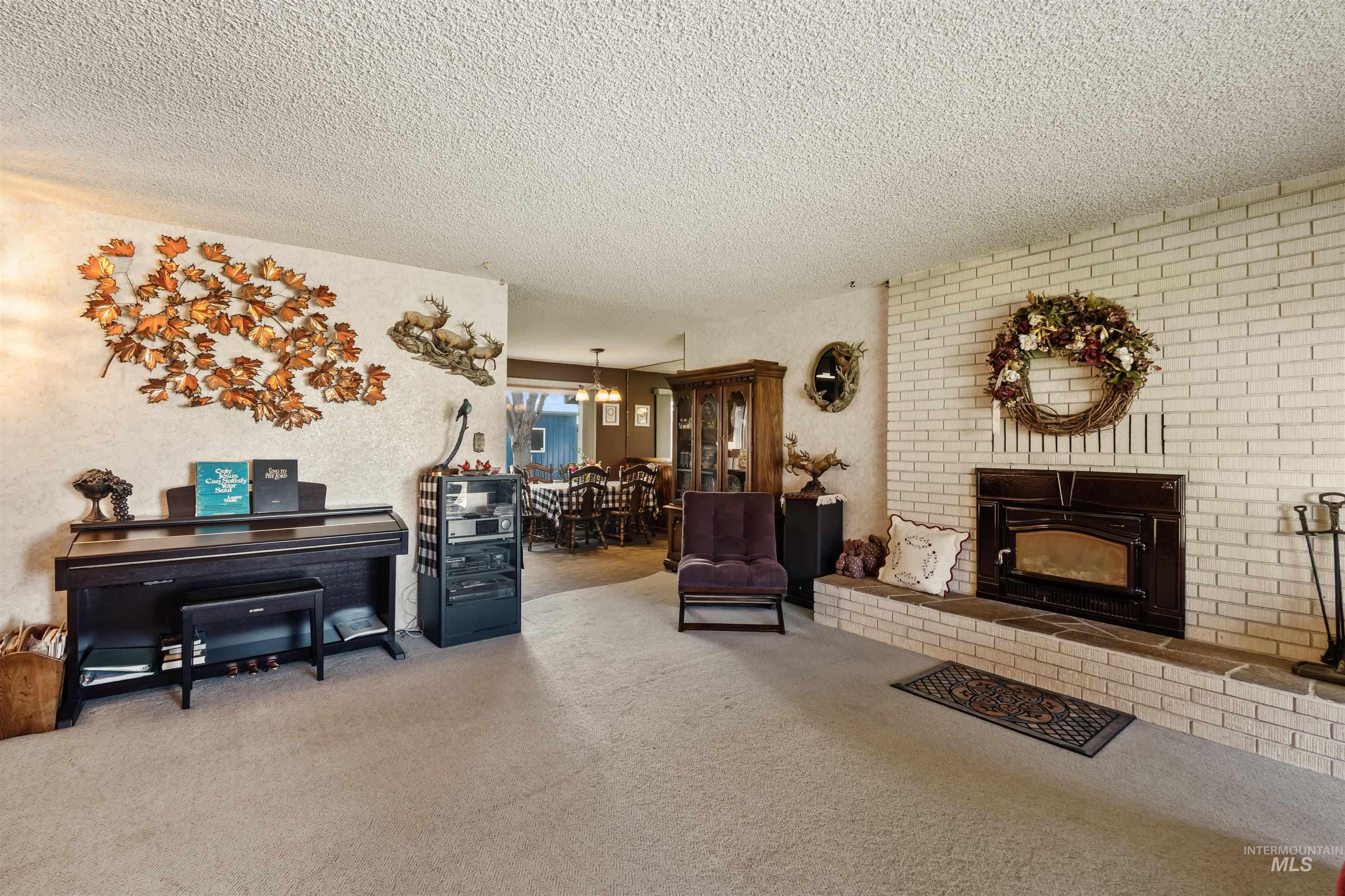 Living room featuring carpet floors, a brick fireplace, a textured ceiling, and a chandelier