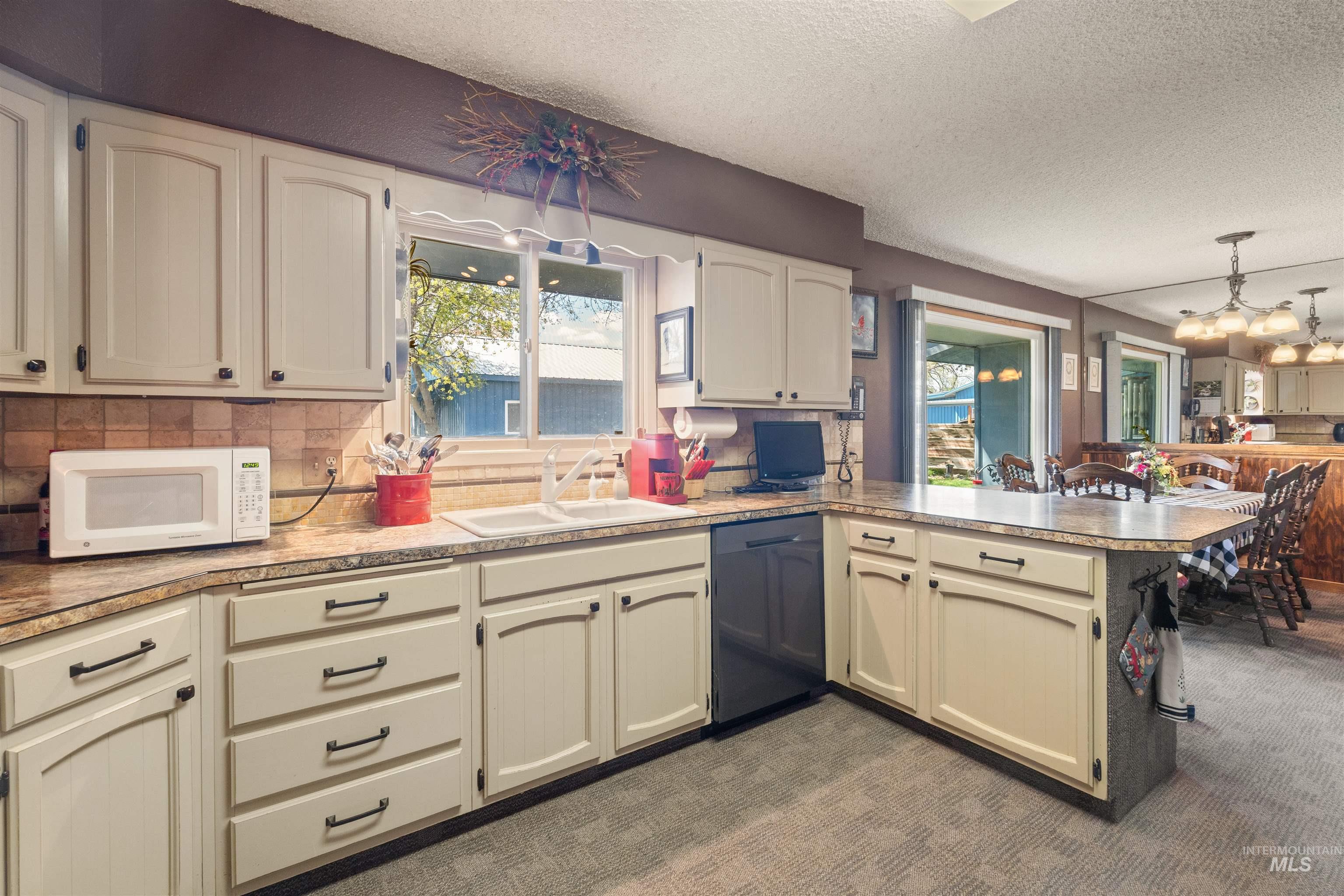 Kitchen featuring a peninsula, a textured ceiling, white microwave, dishwasher, and backsplash