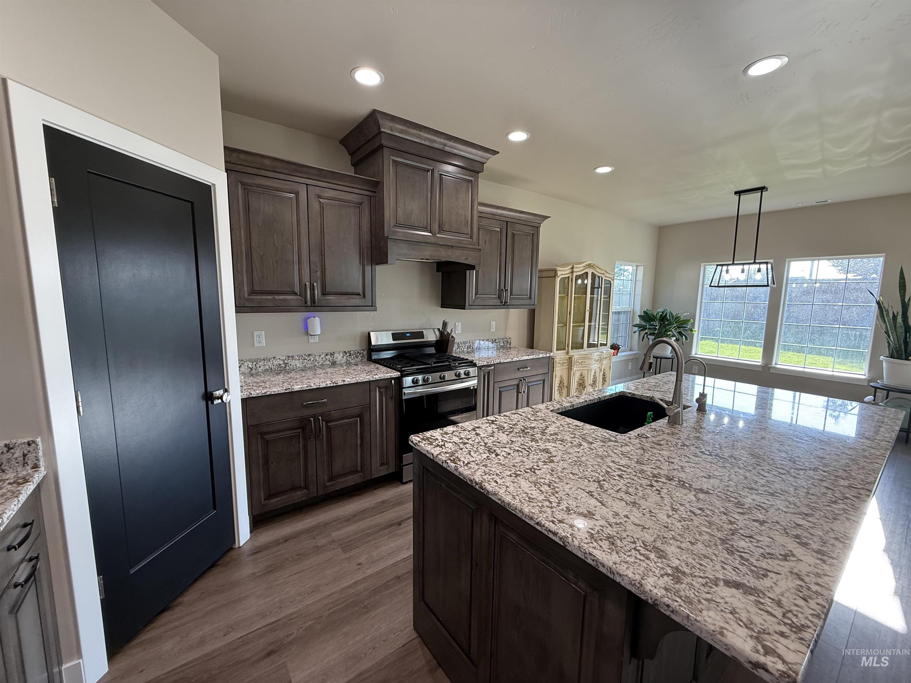 Kitchen featuring stainless steel range with gas stovetop, light stone countertops, hanging light fixtures, recessed lighting, and dark brown cabinetry