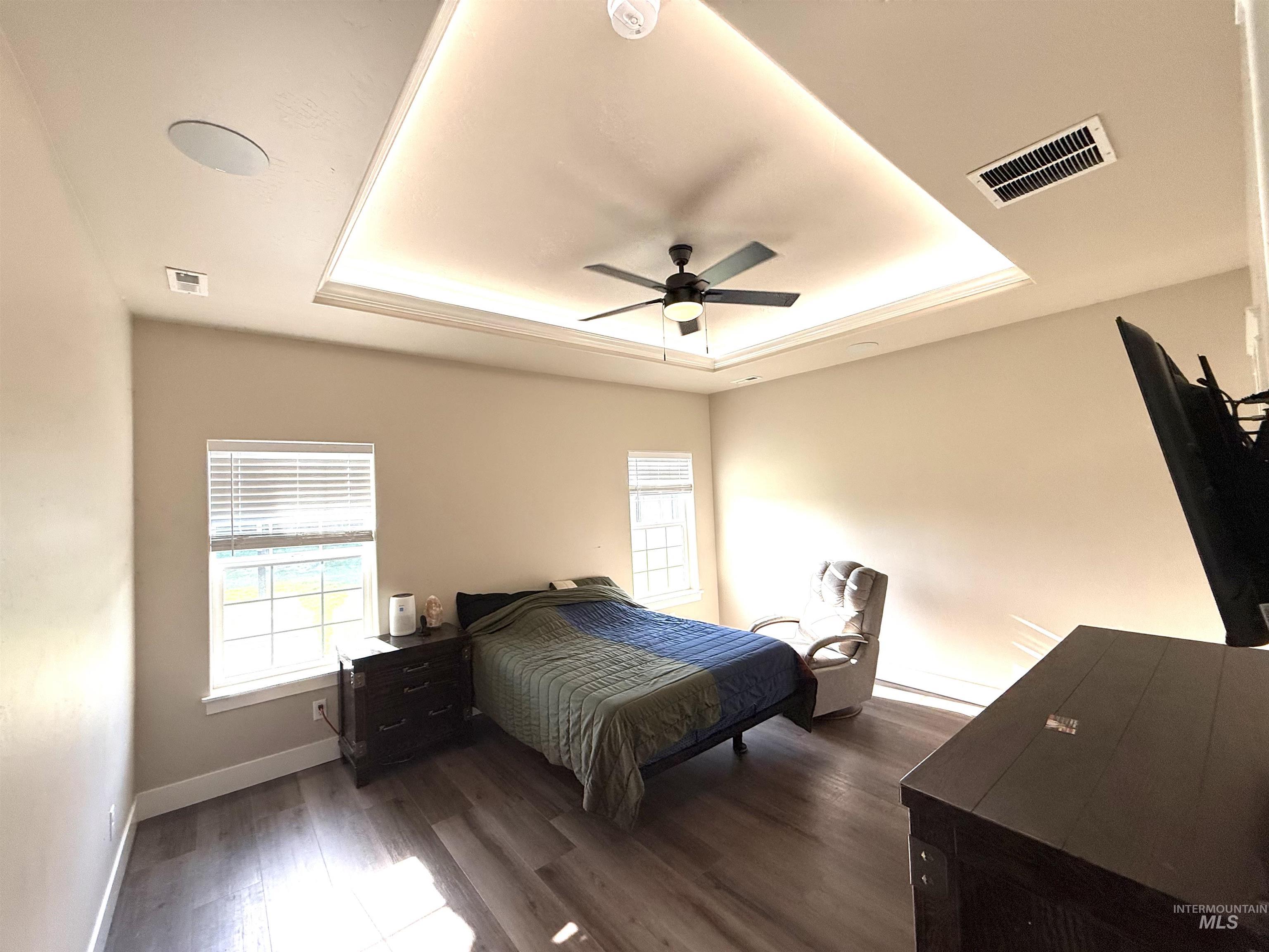 Bedroom featuring a raised ceiling, dark wood finished floors, and ceiling fan