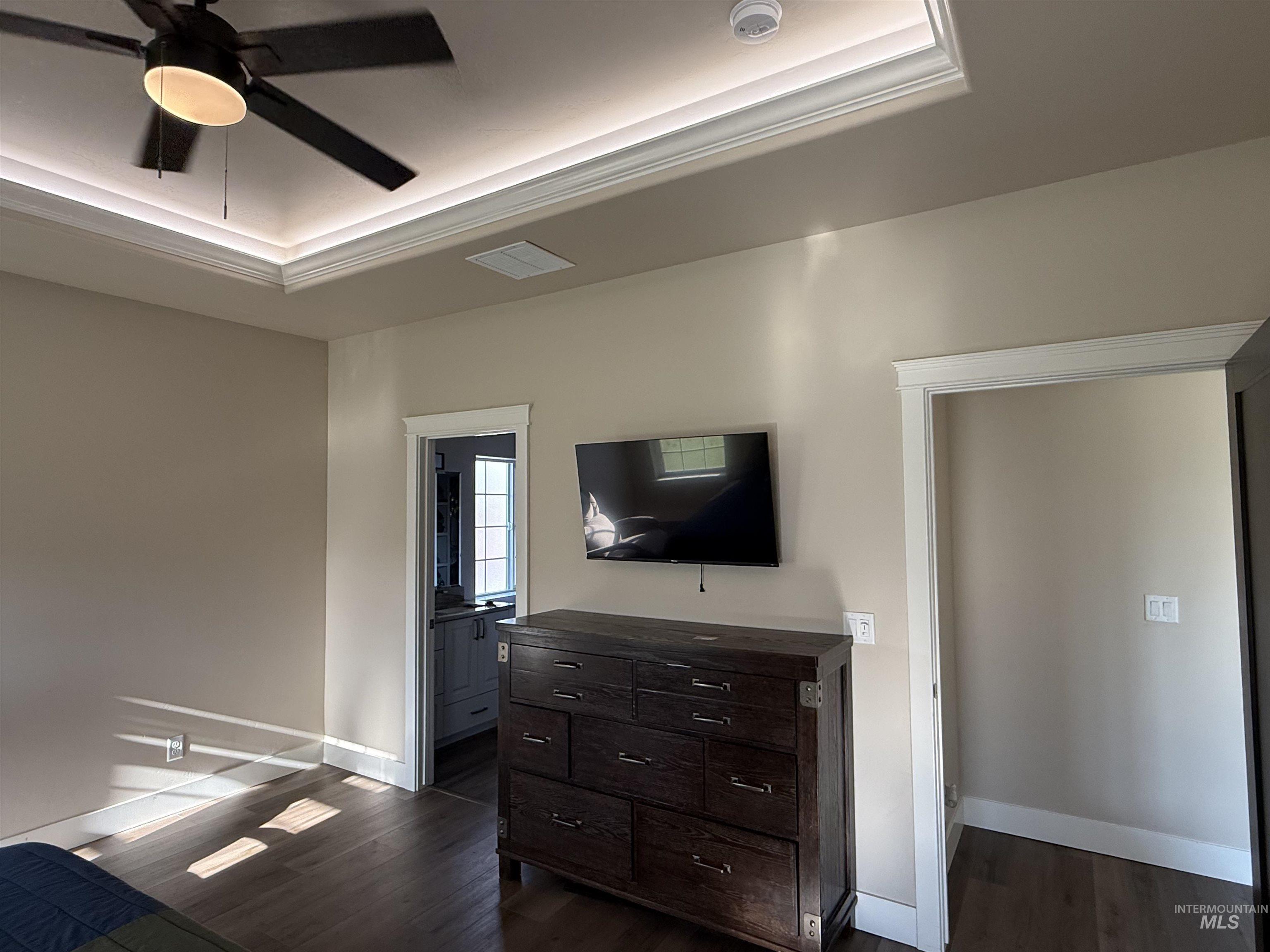 Bedroom with dark wood-type flooring, ceiling fan, crown molding, and a tray ceiling