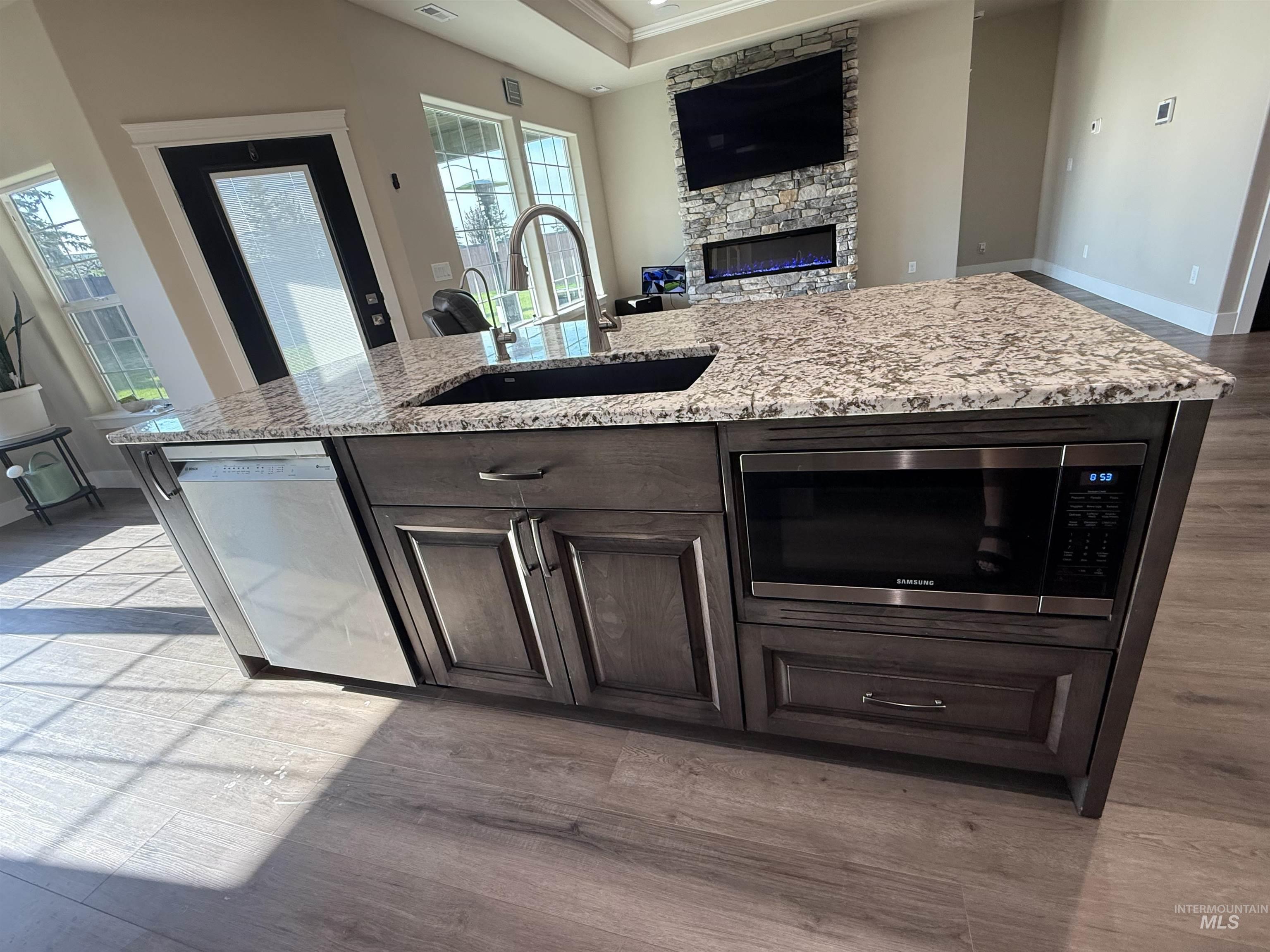 Kitchen featuring light wood finished floors, dark brown cabinets, a fireplace, appliances with stainless steel finishes, and a kitchen island with sink