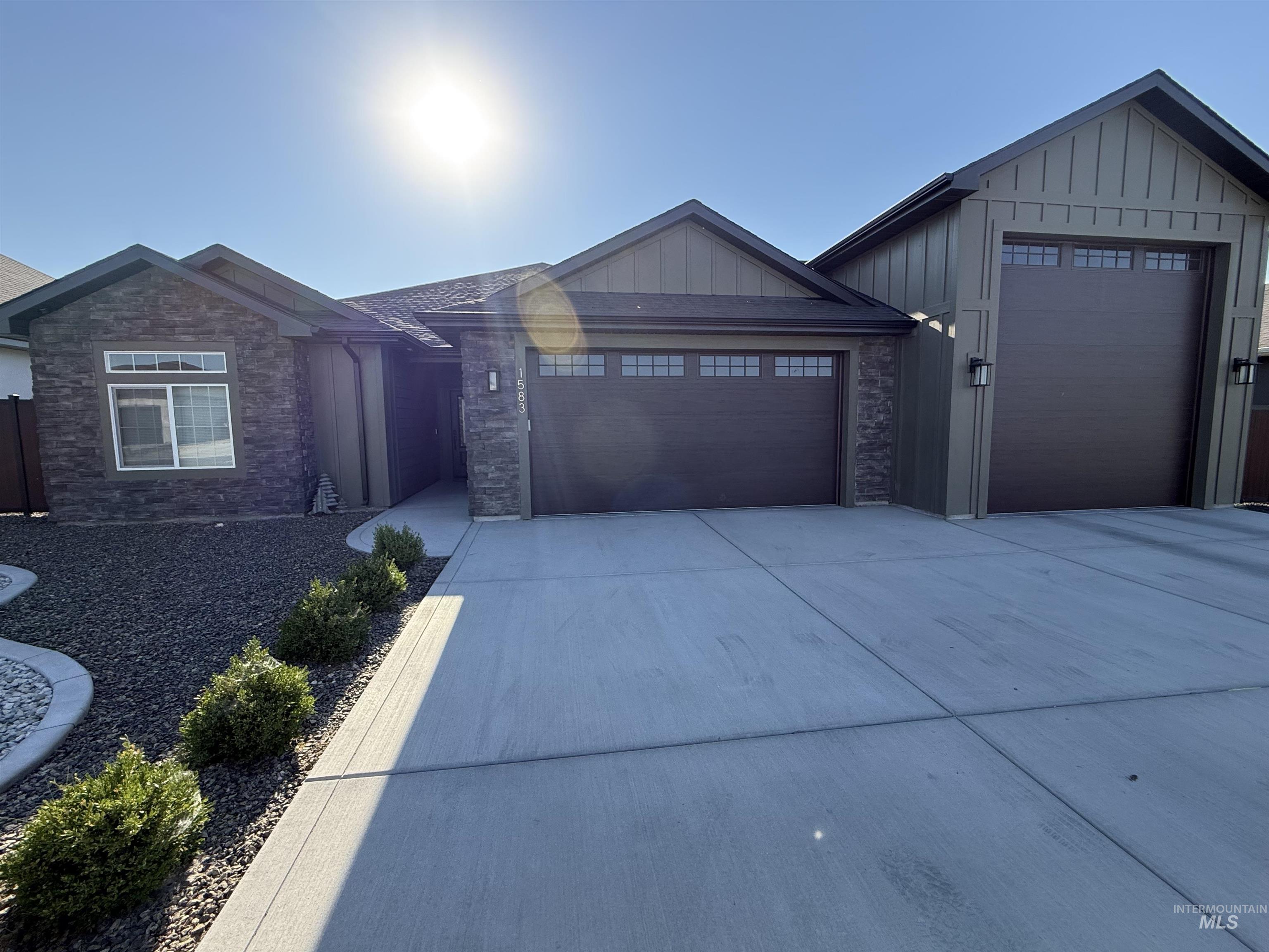 View of front of property featuring board and batten siding, a garage, concrete driveway, and stone siding