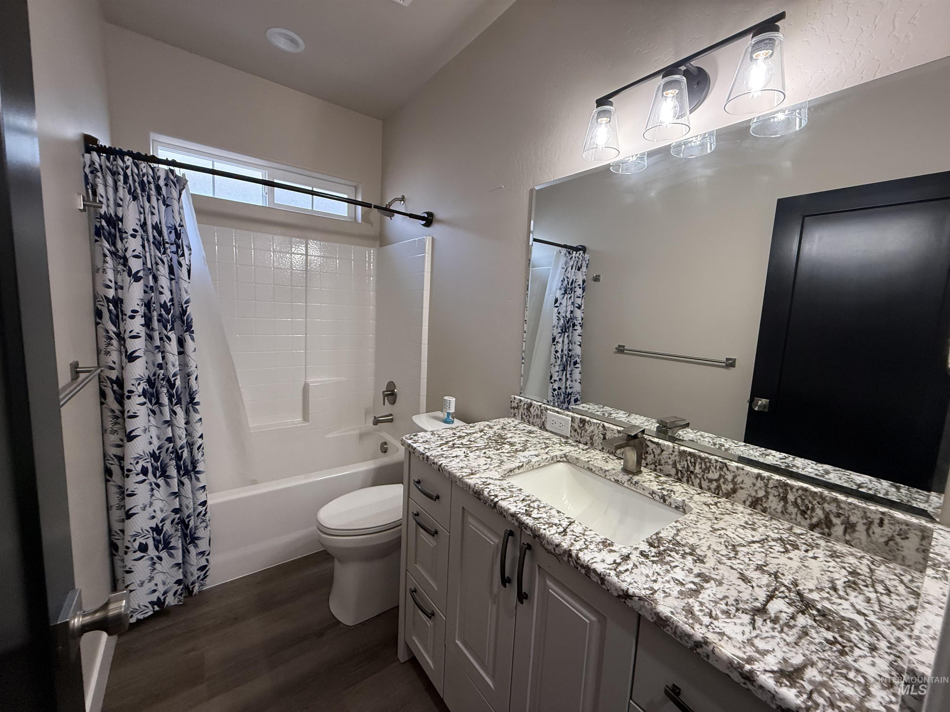 Full bathroom featuring vanity, shower / bath combo with shower curtain, and dark wood-style floors