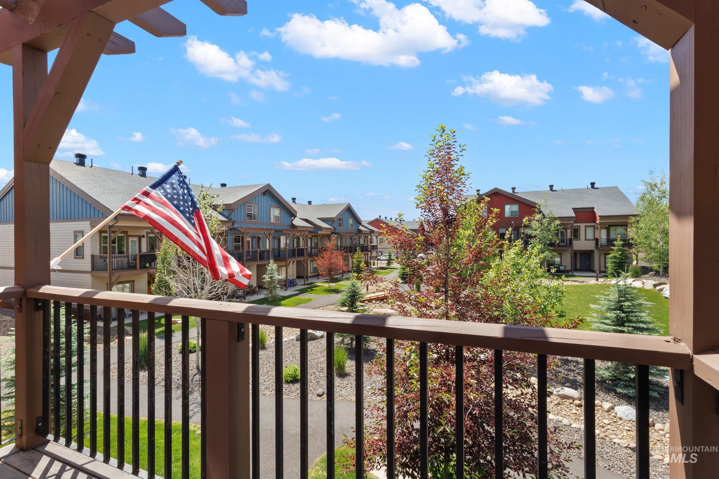 Balcony with dark wood railing and pergola, overlooking a landscaped courtyard with mature trees, paved pathways, and green spaces