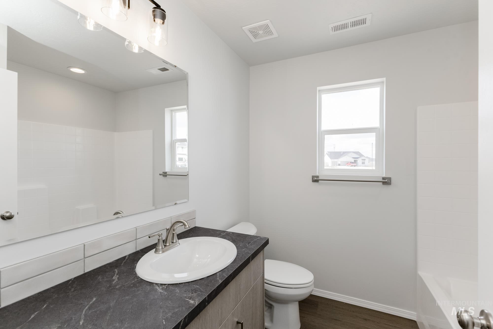 Bathroom with healthy amount of natural light, vanity, dark wood-style flooring, and washtub / shower combination