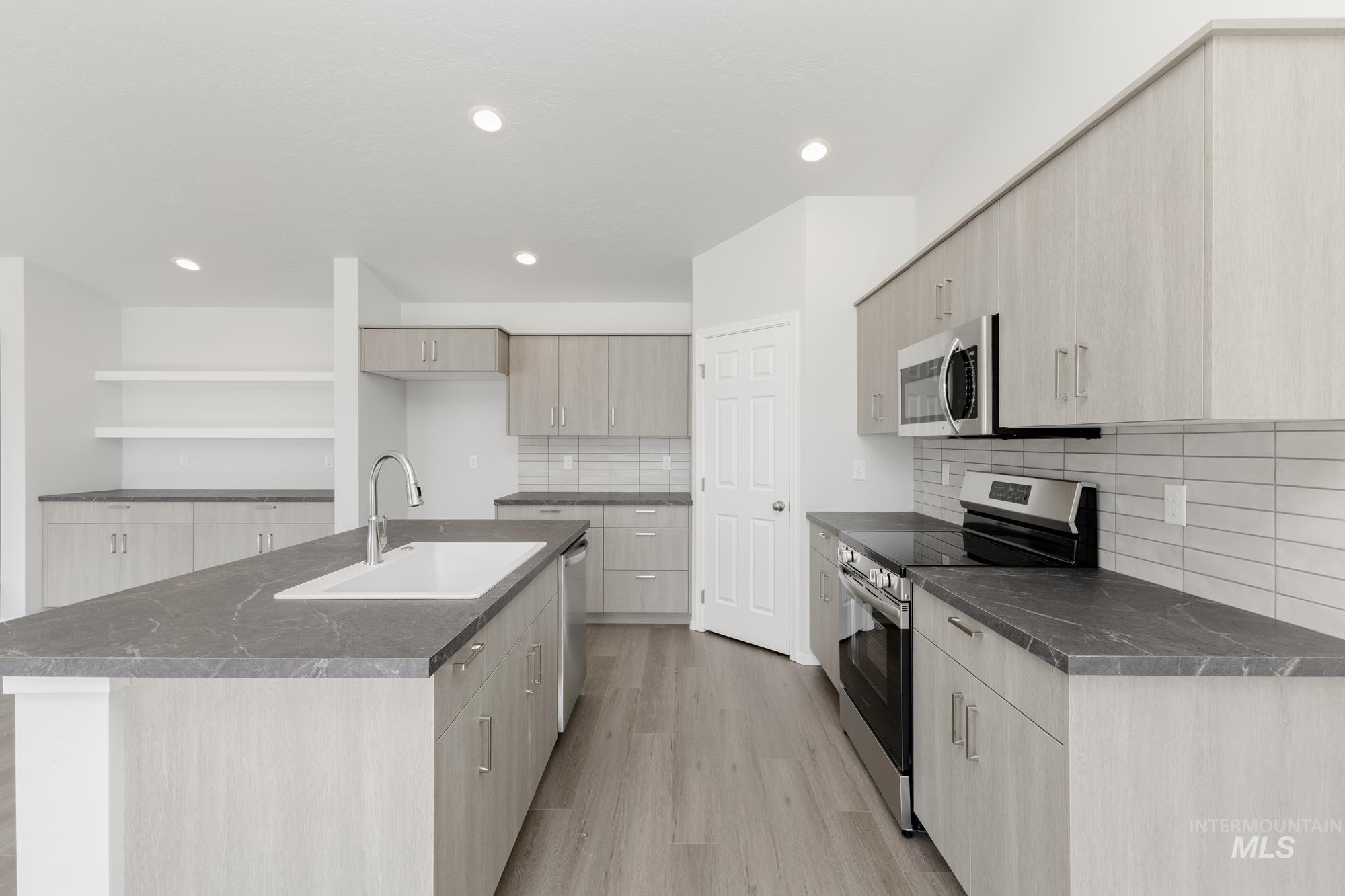 Kitchen with stainless steel appliances, light wood-style flooring, open shelves, an island with sink, and tasteful backsplash