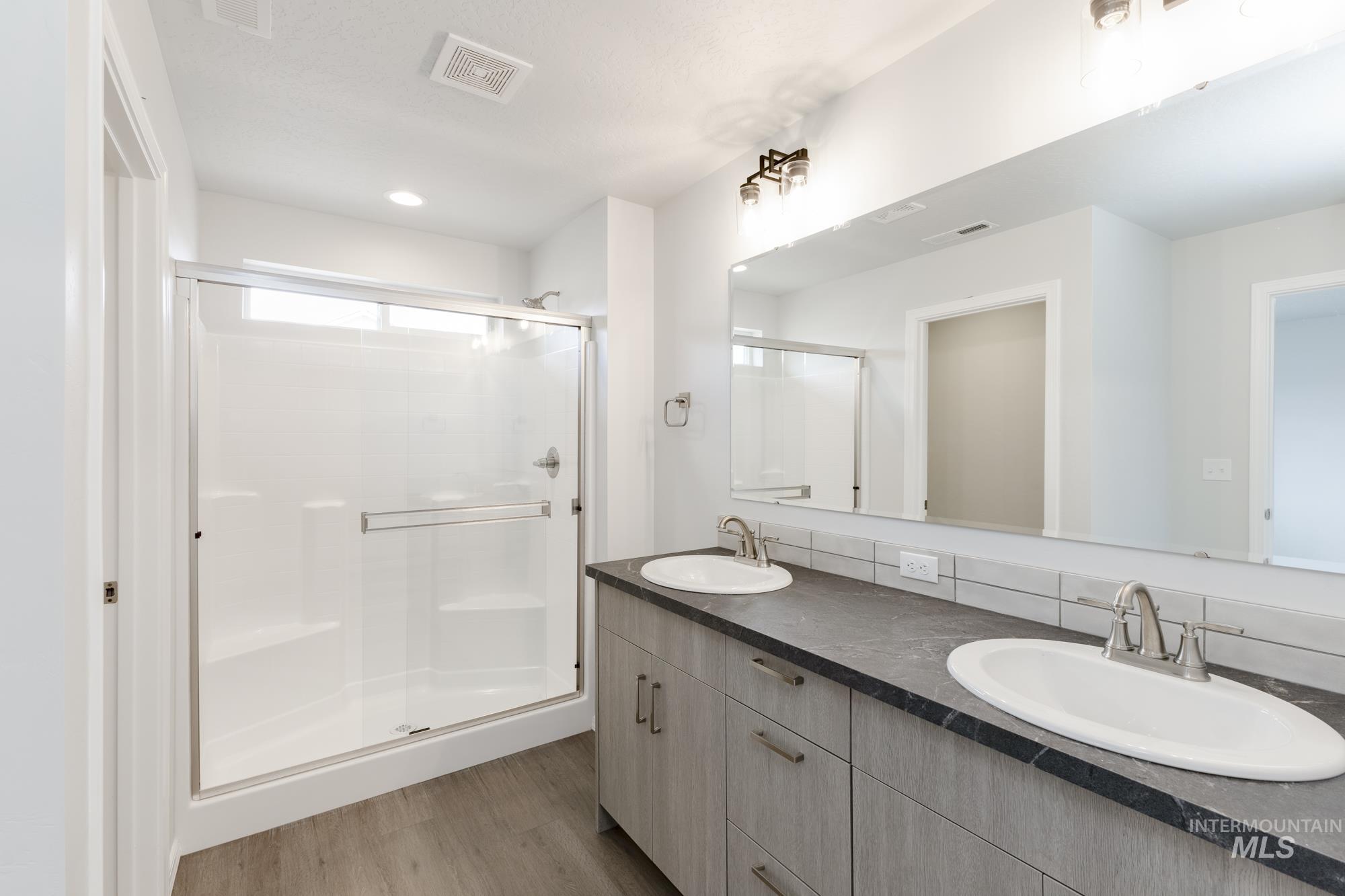 Full bath featuring double vanity, light wood-style flooring, a shower stall, and recessed lighting