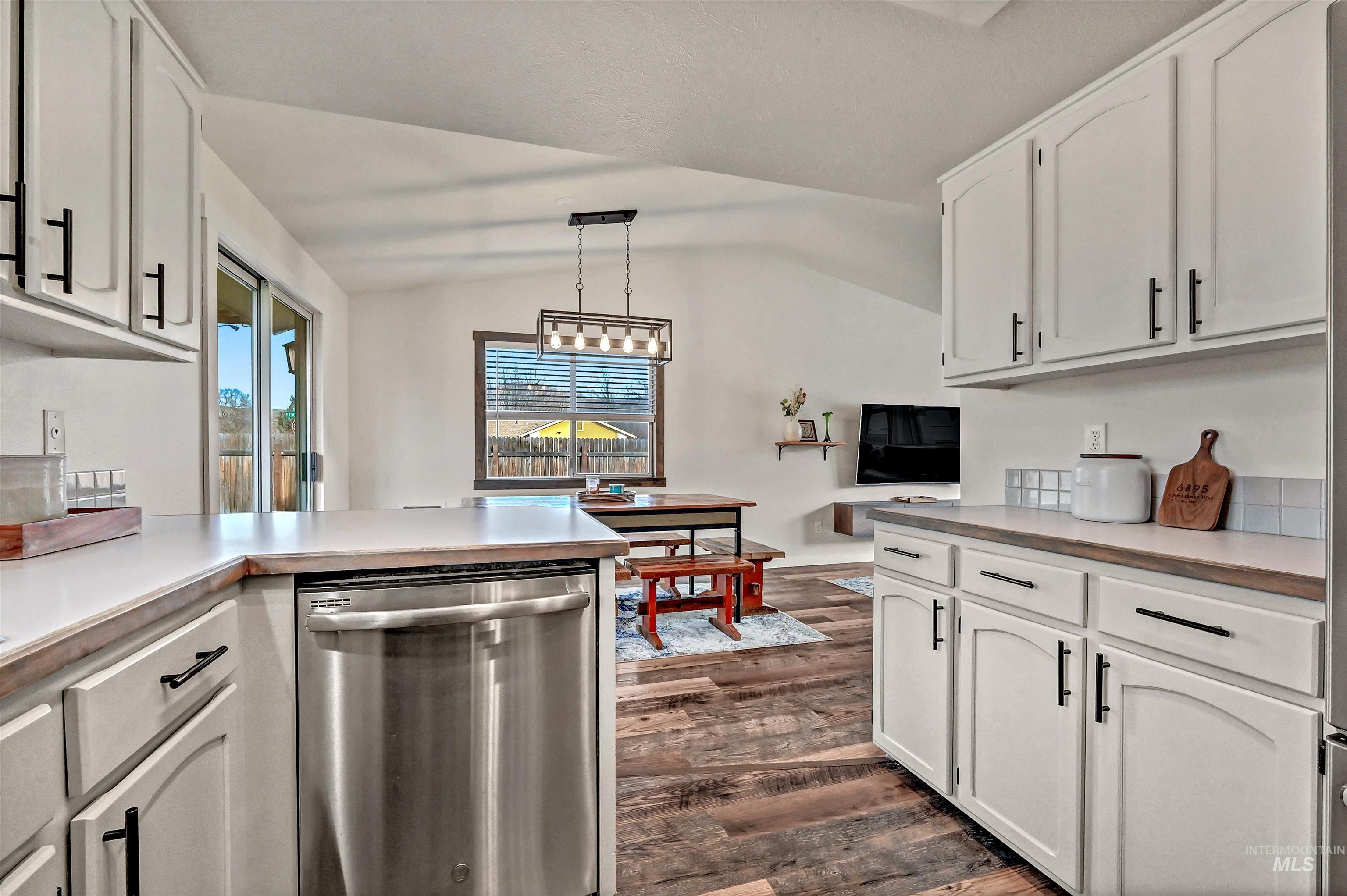 Kitchen with stainless steel dishwasher, lofted ceiling, light countertops, dark wood finished floors, and white cabinets