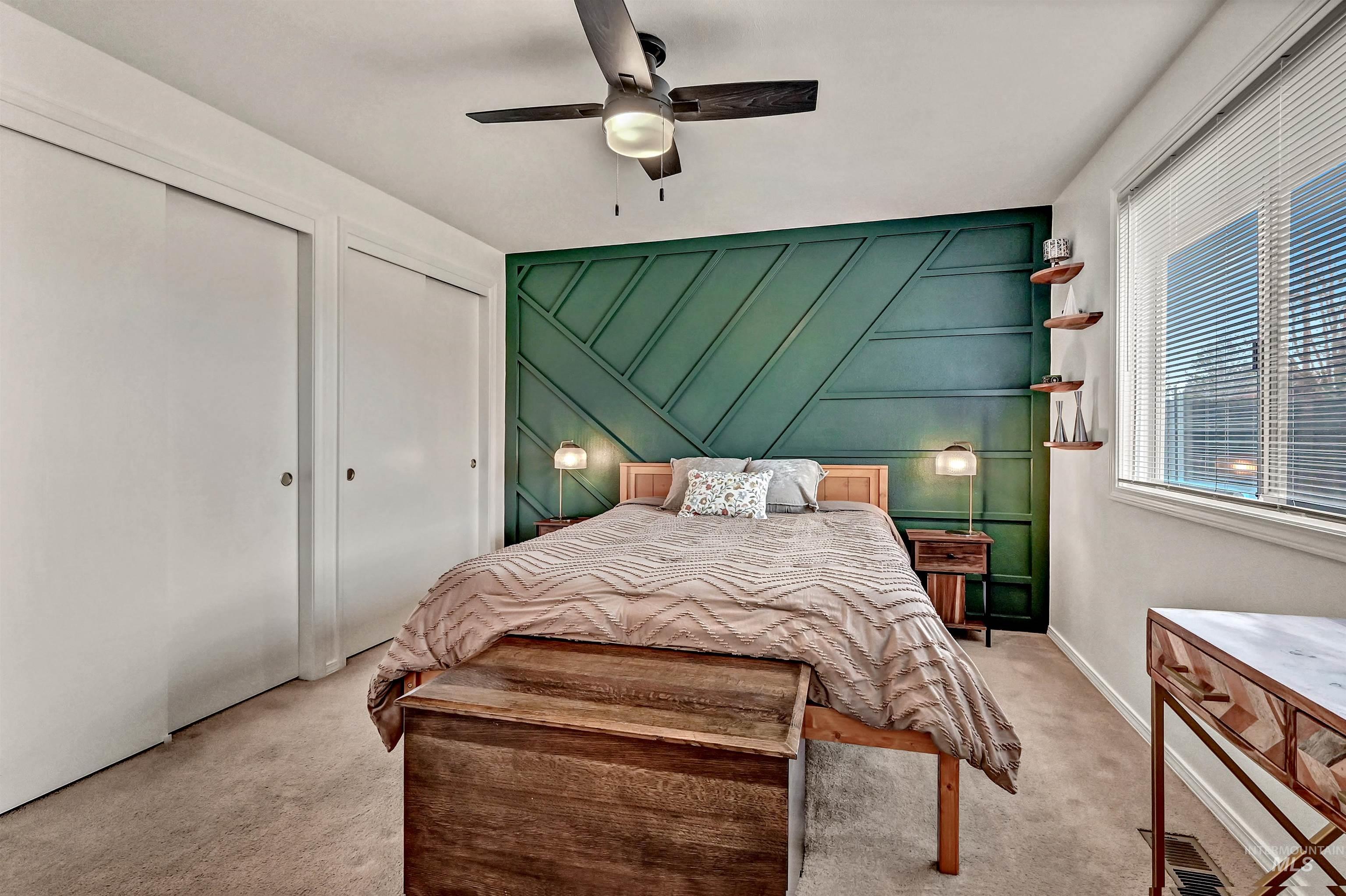 Bedroom with two closets, a decorative wall, an accent wall, carpet flooring, and ceiling fan