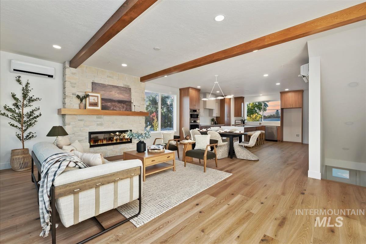 Open-concept living space featuring wood-finish flooring, exposed ceiling beams, recessed lighting, and a stone-clad fireplace with a natural wood mantel