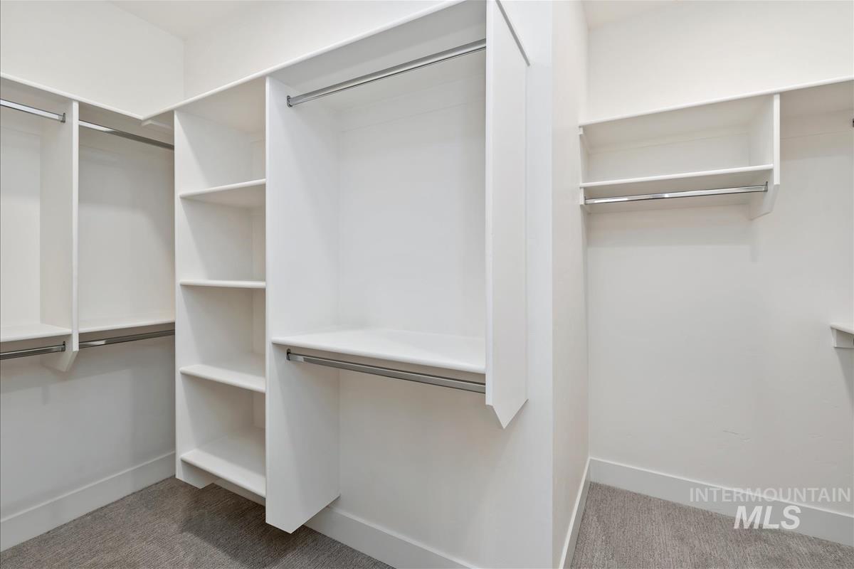 Walk-in closet featuring white built-in shelving, multiple hanging rods, and light gray carpet flooring