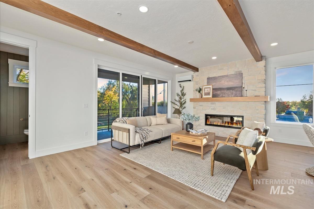 Spacious living area featuring exposed wood-finish ceiling beams, light wood-finish flooring, and a stone-clad fireplace with a wood mantel