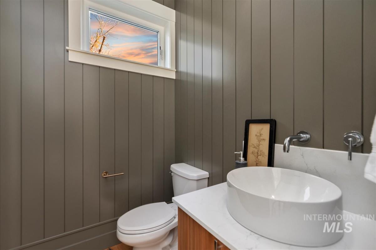 Powder room featuring vertical wall paneling, a contemporary oval vessel sink, wall-mounted chrome faucet, and a white countertop with integrated backsplash