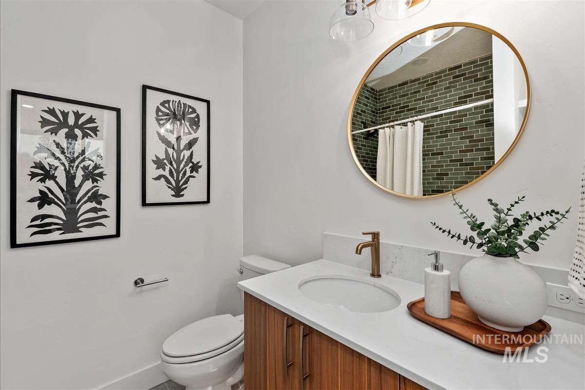 Bathroom featuring a wood-finish vanity with a white countertop and integrated sink, a gold-framed circular mirror, a gold-finish faucet, and a shower with green subway tile surround