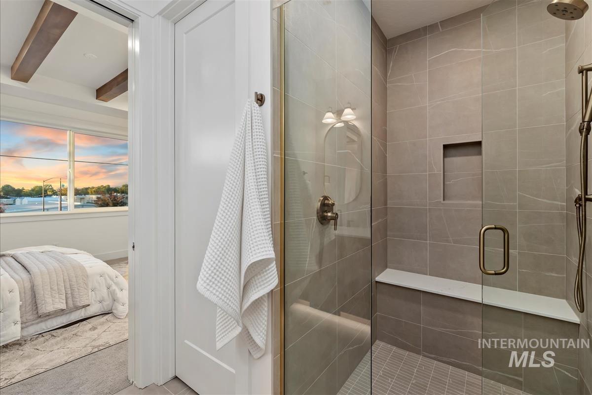 Walk-in shower featuring glass enclosure with brass accents, large format tile walls, built-in tile bench, and recessed shelf