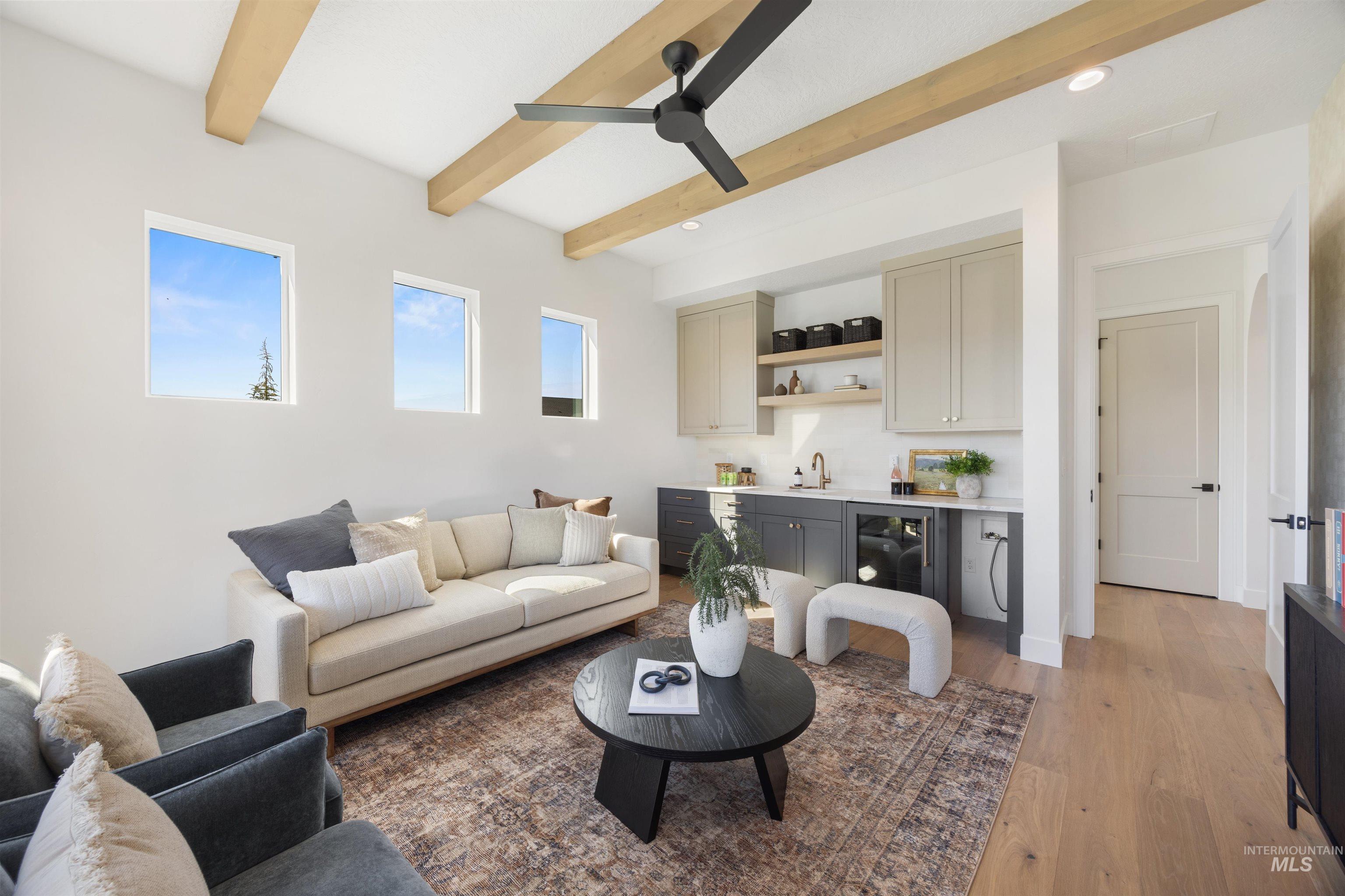 Living area with light wood finished floors, beamed ceiling, bar with sink, recessed lighting, and wine cooler