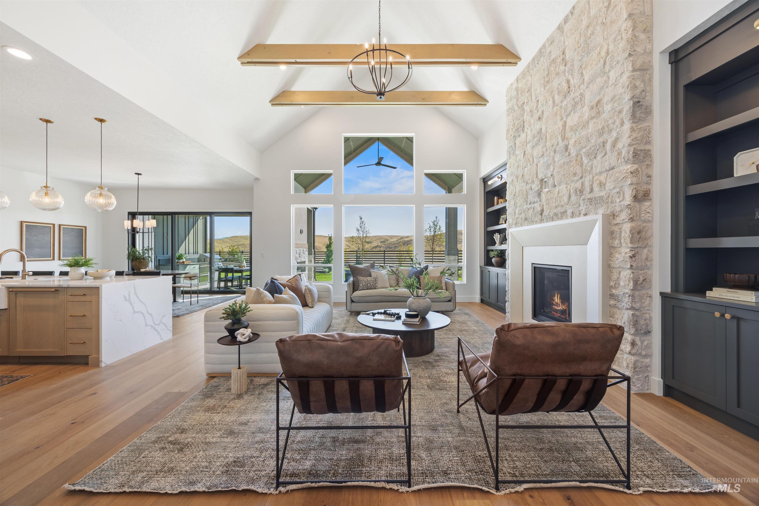 Living room featuring a chandelier, built in features, light wood finished floors, beam ceiling, and a stone fireplace