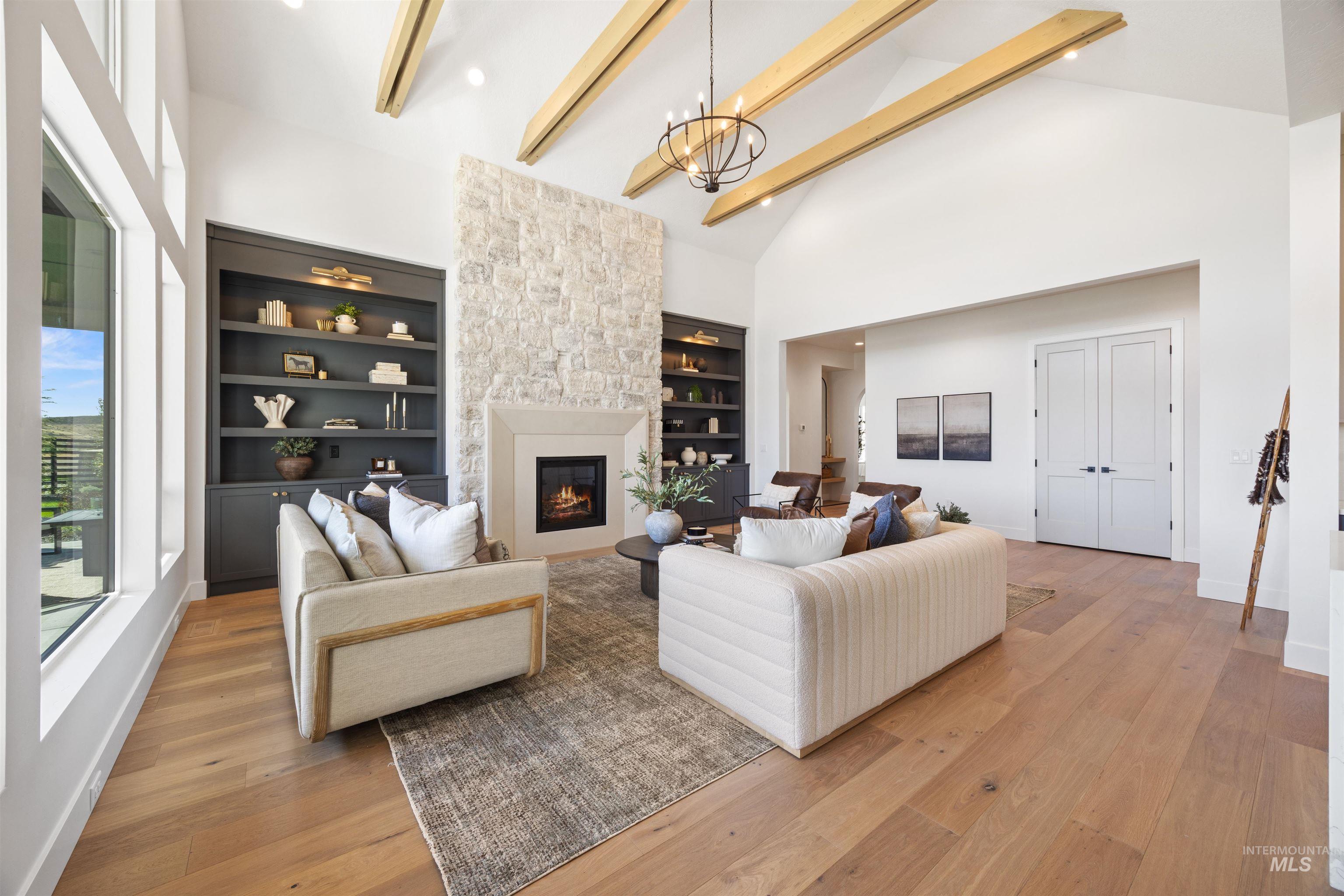 Living area featuring high vaulted ceiling, light wood-type flooring, beamed ceiling, a fireplace, and a chandelier