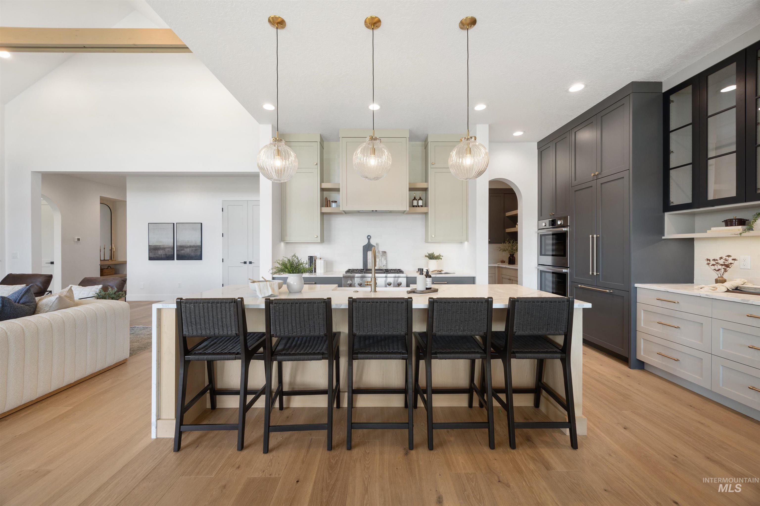Kitchen featuring arched walkways, open shelves, a breakfast bar area, hanging light fixtures, and light wood-style floors