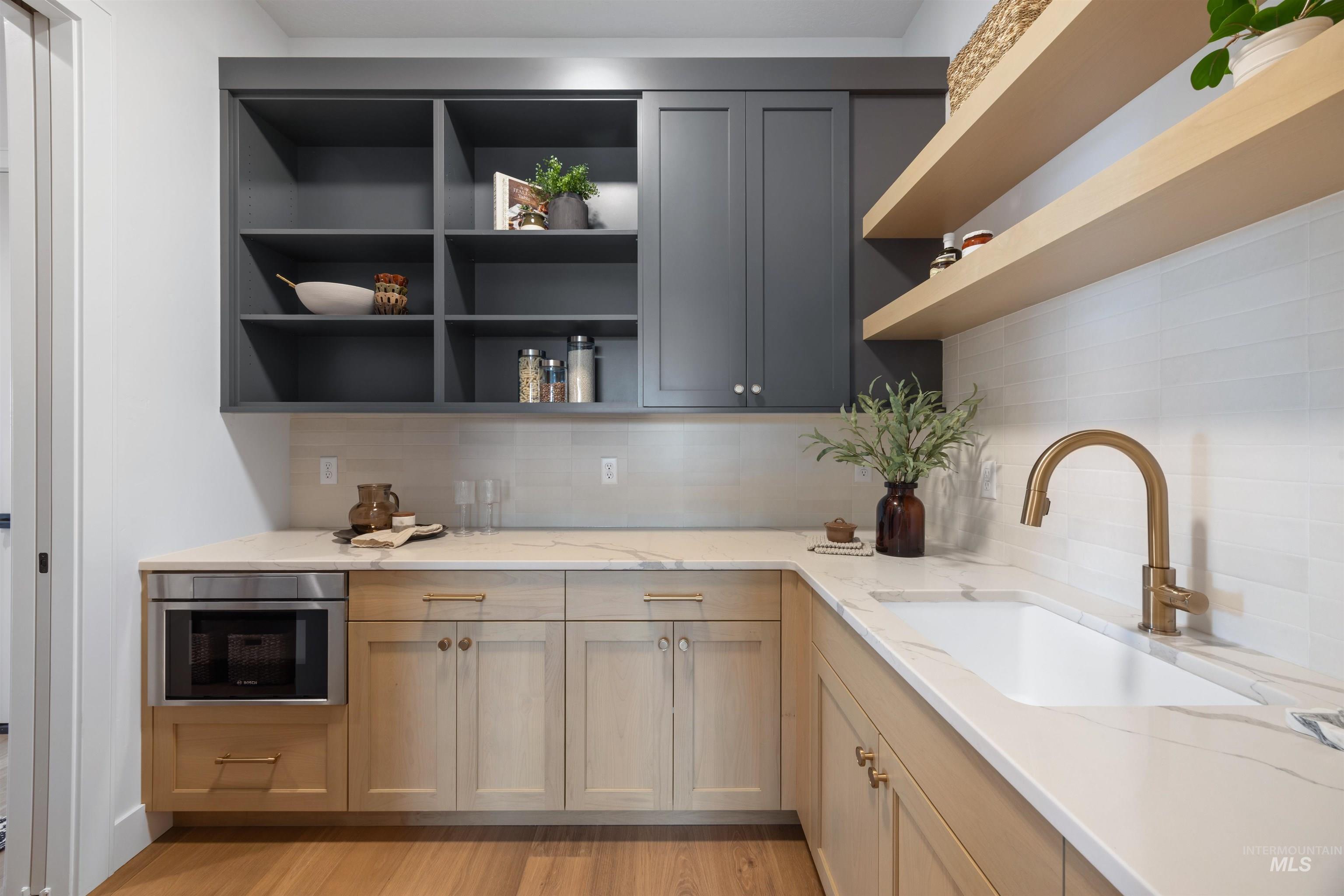 Kitchen with open shelves, tasteful backsplash, light wood-type flooring, light stone countertops, and stainless steel microwave