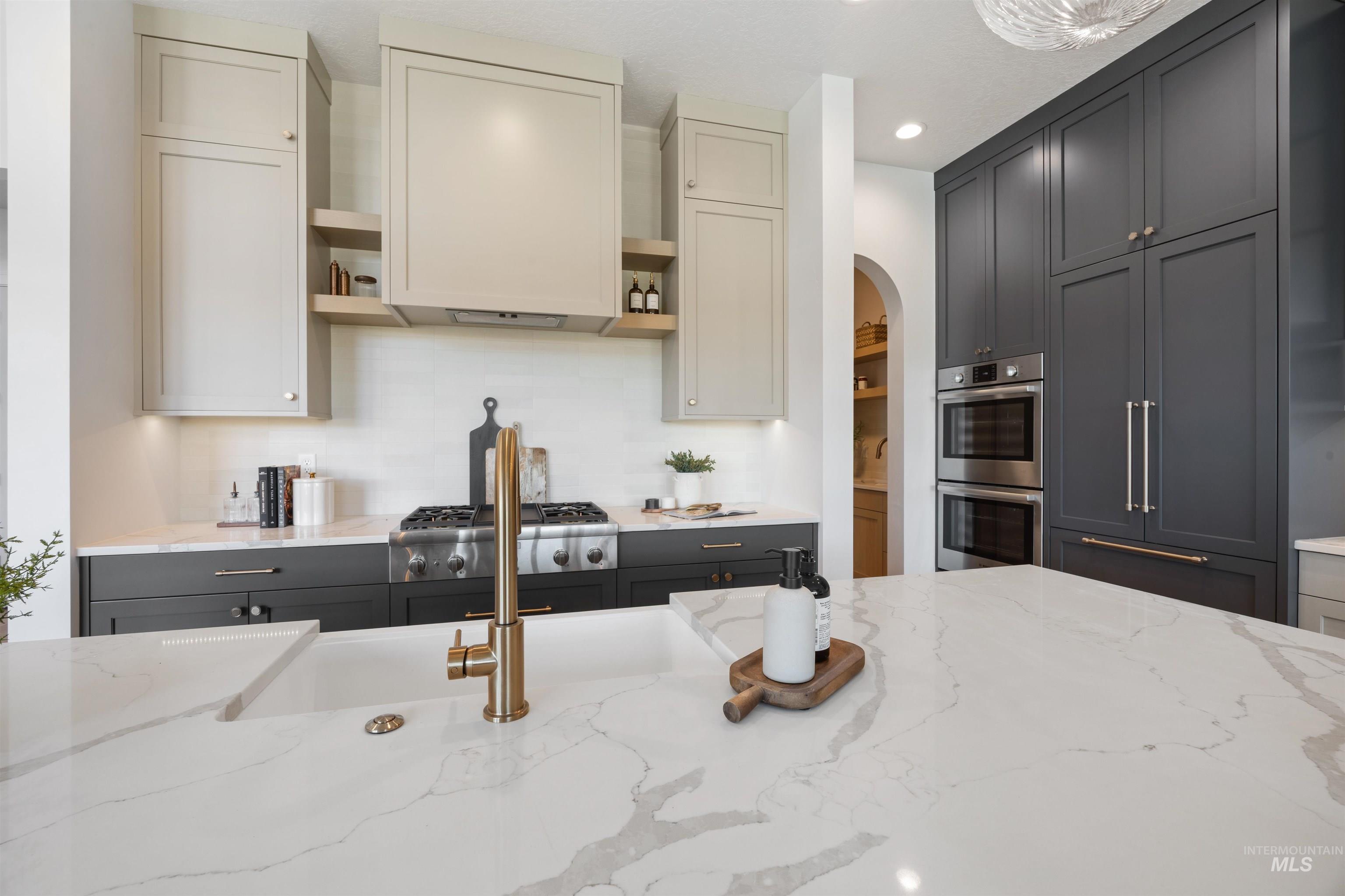 Kitchen with open shelves, light stone countertops, arched walkways, stainless steel appliances, and gray cabinetry