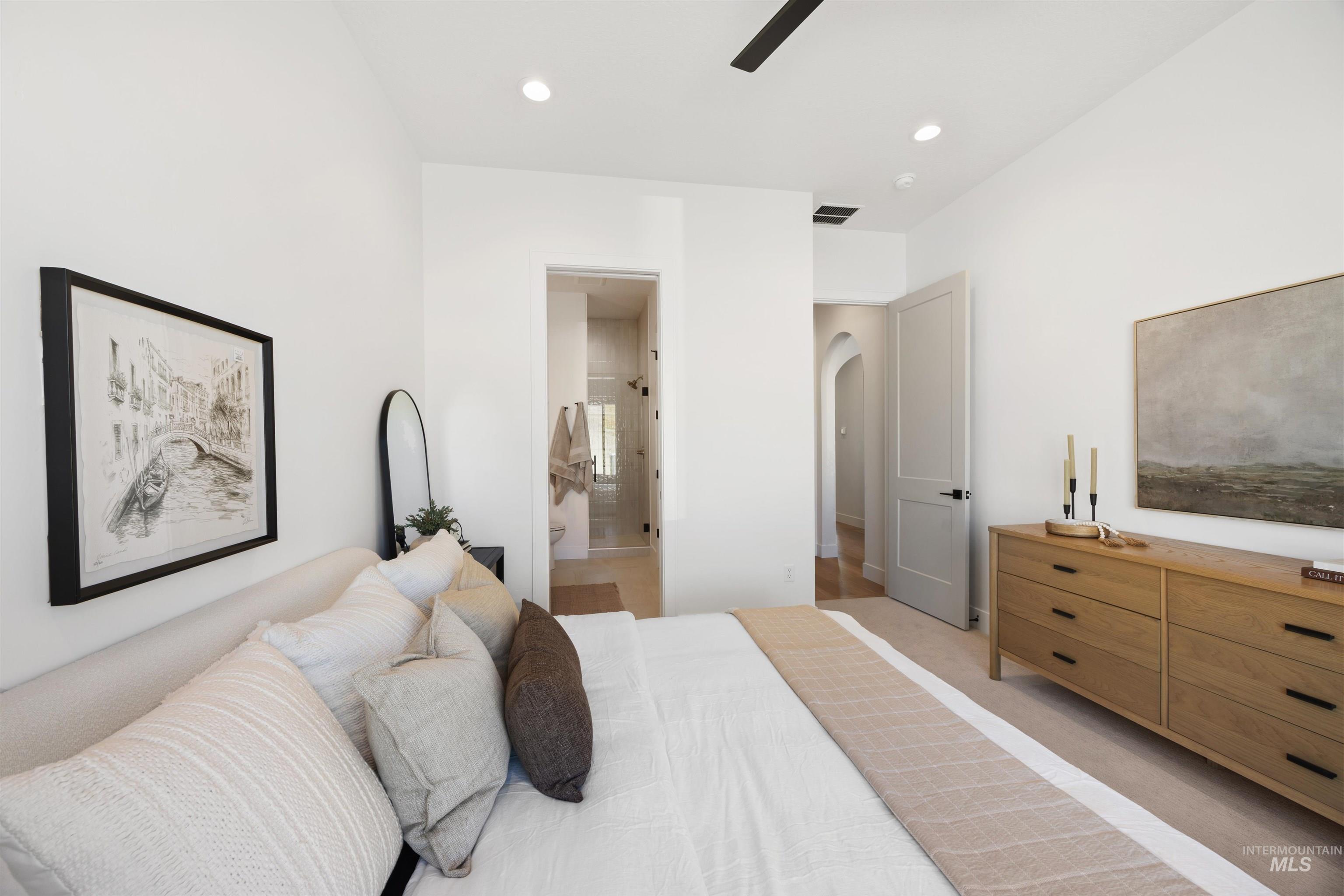 Bedroom featuring light carpet, connected bathroom, arched walkways, recessed lighting, and a ceiling fan