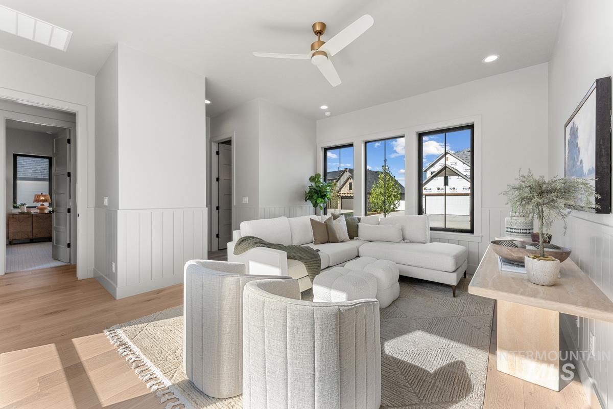 Living room with light wood finished floors, a ceiling fan, a wainscoted wall, and recessed lighting