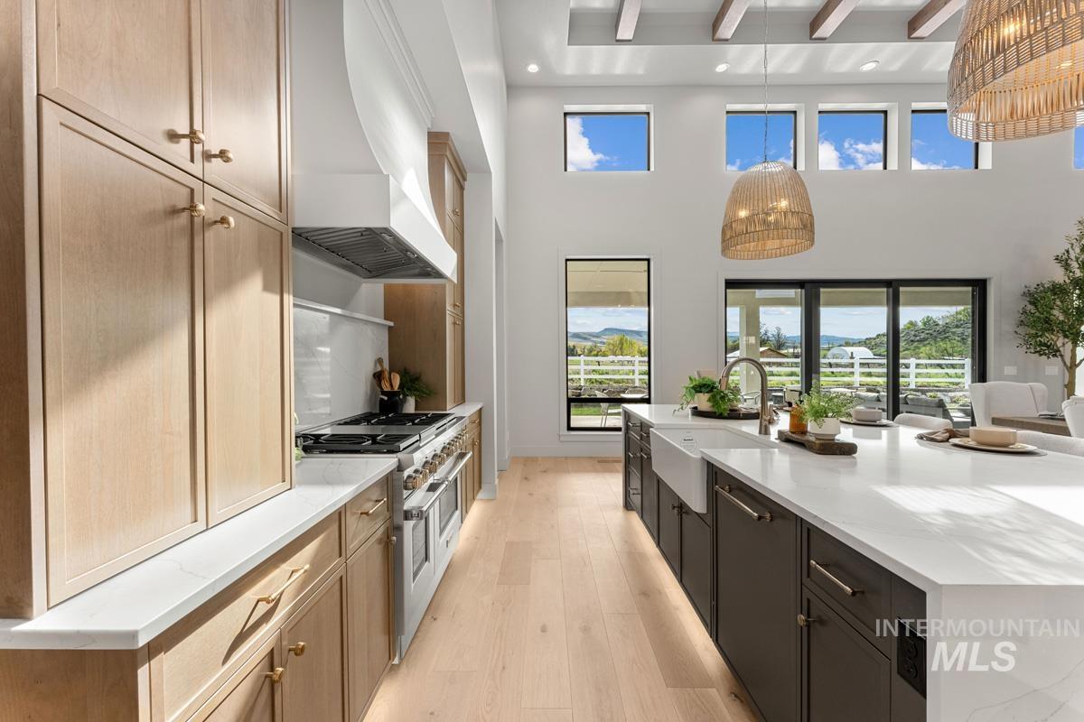 Two tone kitchen featuring light wood-type flooring, light stone countertops, range with two ovens, a spacious island, and plenty of natural light