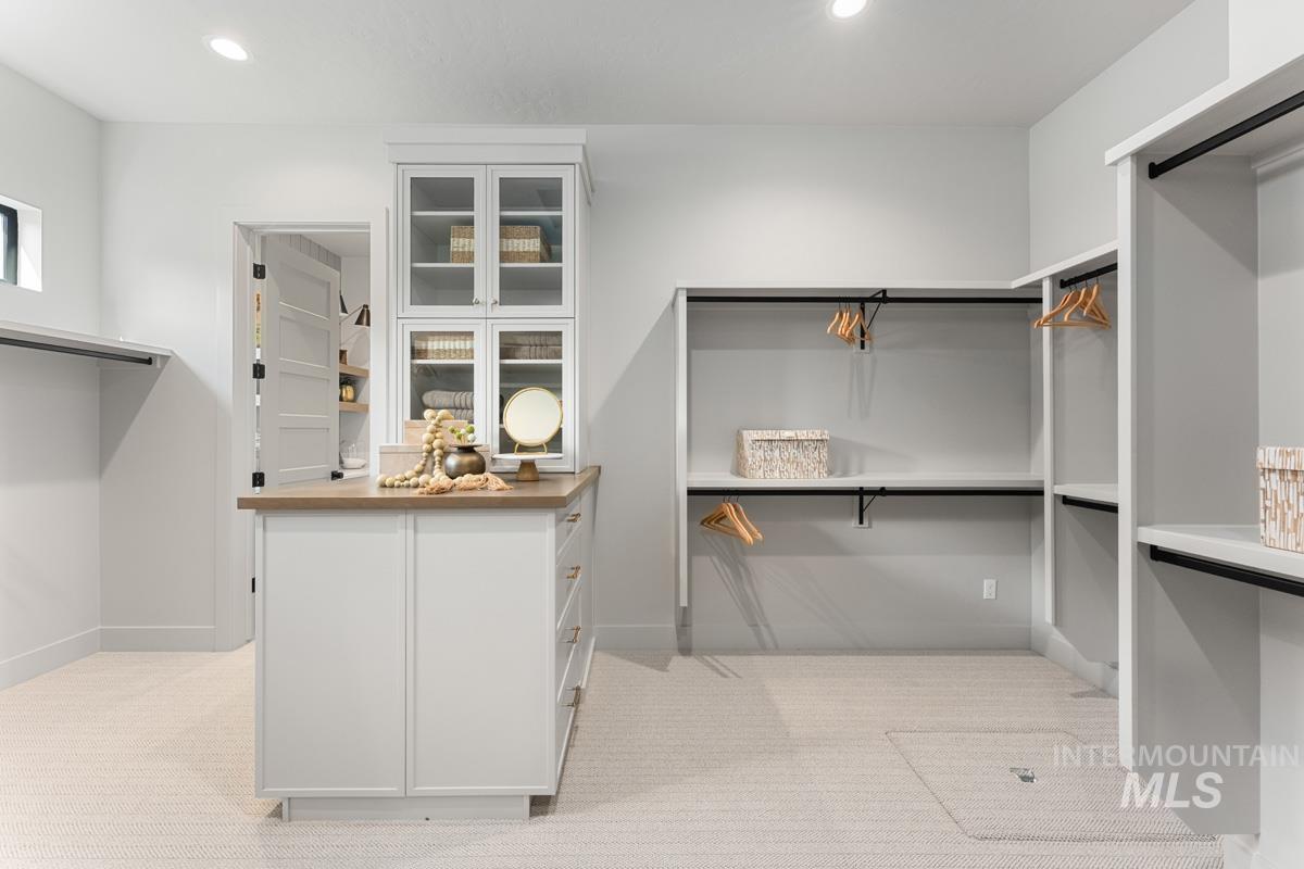 Spacious walk-in closet featuring a central island with wood-finish countertop and glass-front upper cabinetry