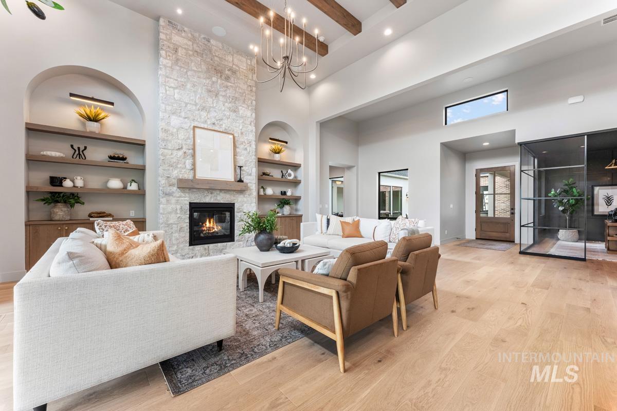 Living room featuring light wood-style floors, a stone fireplace, hanging lights, and built in shelves