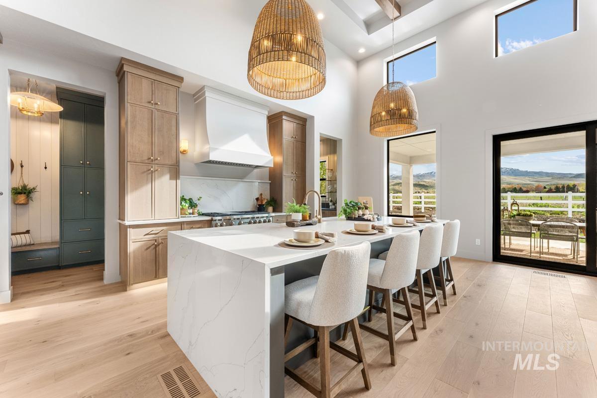 Kitchen featuring a kitchen bar, light wood-style floors, an island with sink, light stone counters, and a high ceiling