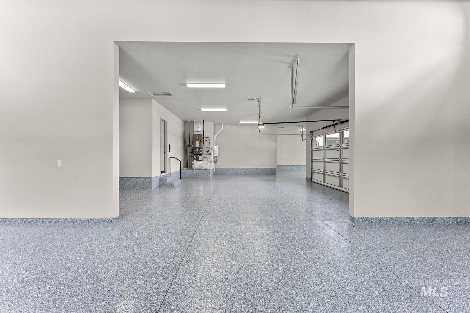 Spacious garage featuring a durable epoxy floor coating, ample overhead lighting, and an overhead garage door with multiple panels