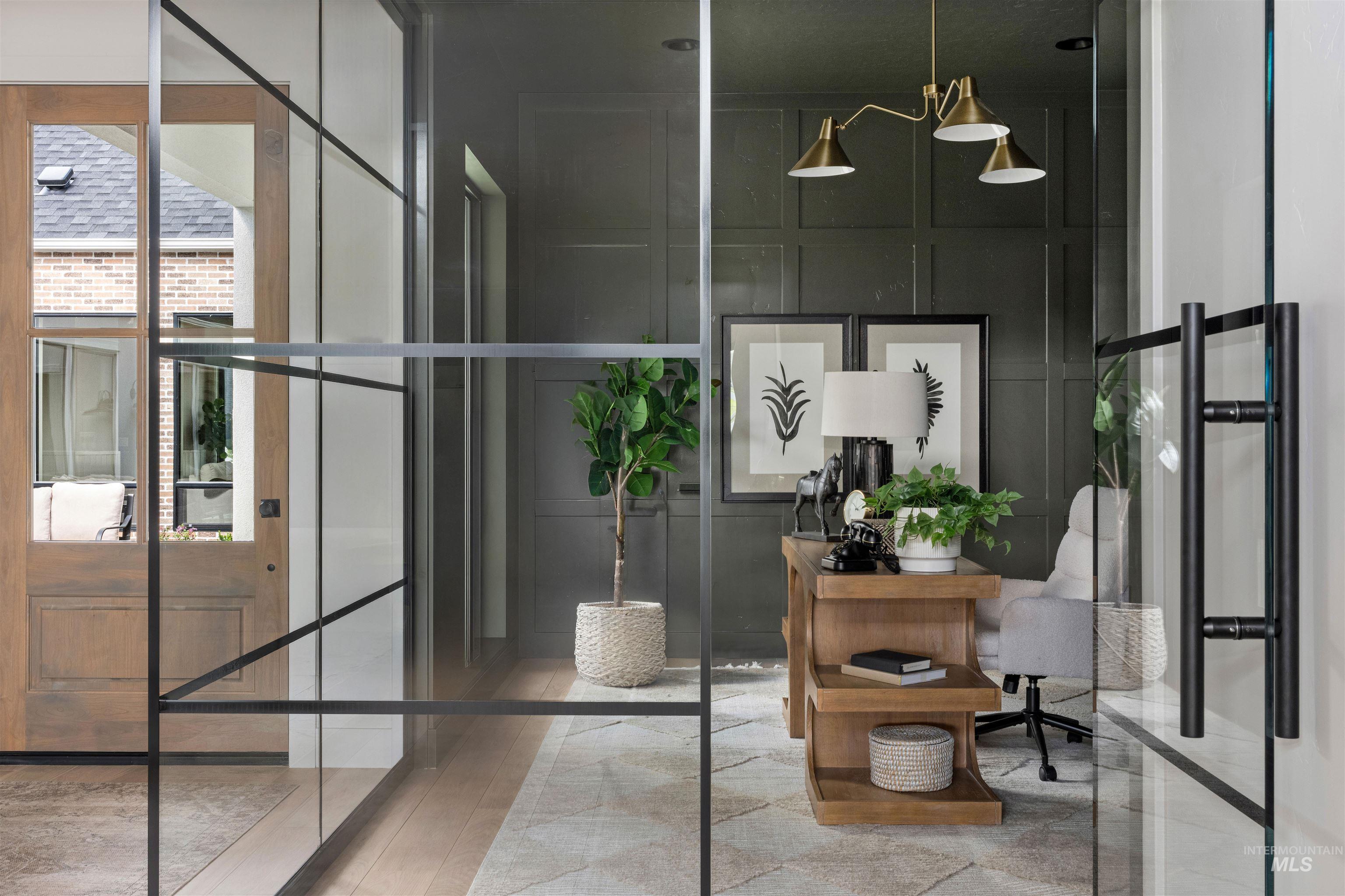 Glass-paneled entryway with a wood-finish door and a room featuring dark paneled walls, a brass multi-arm chandelier, and a light wood desk