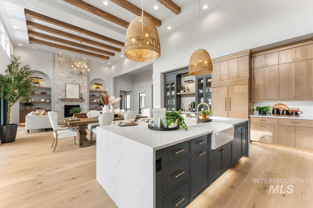 Kitchen featuring two tone cabinets, light stone counters, a center island with sink, open floor plan, and a large fireplace