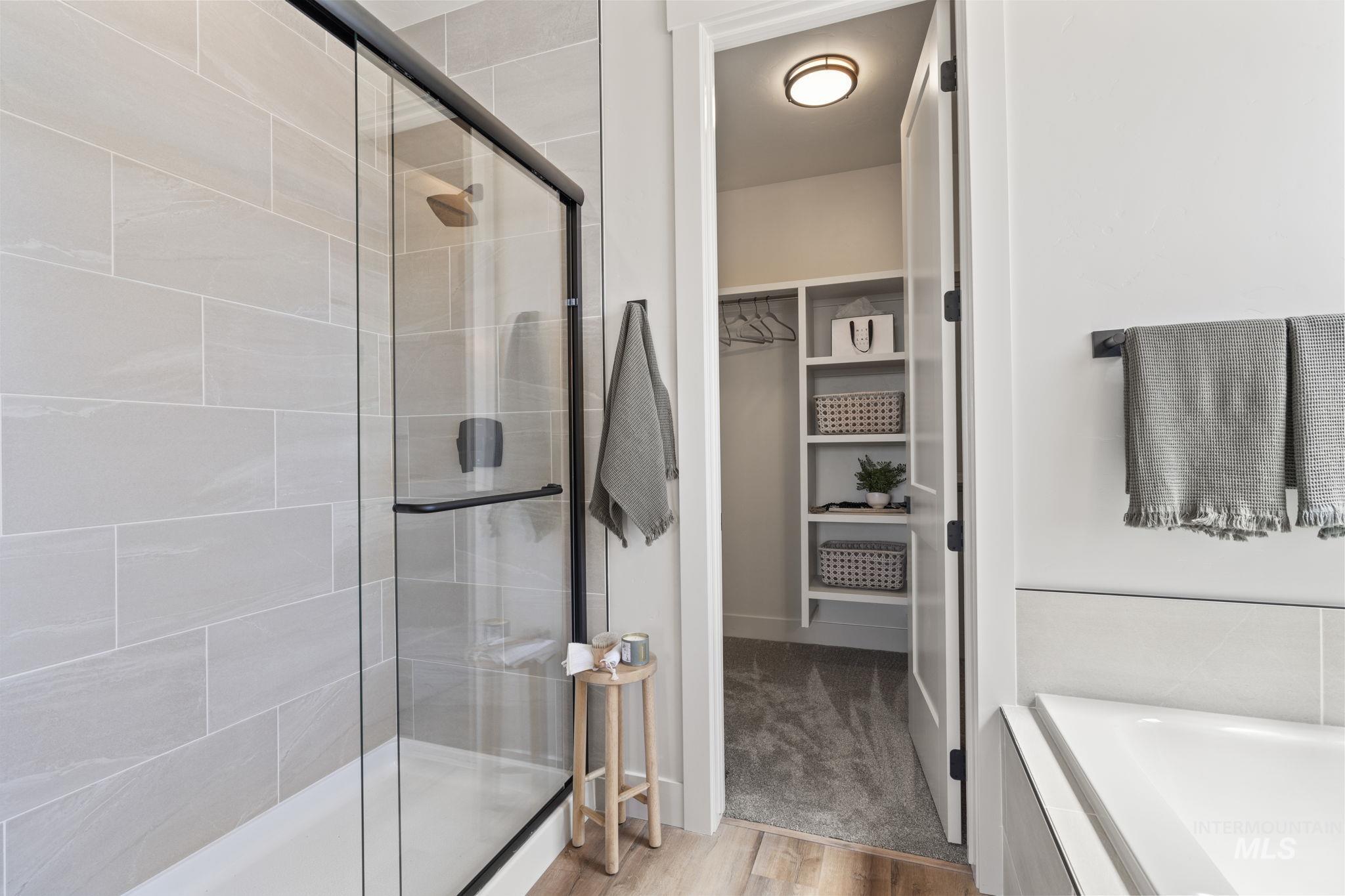 Bathroom featuring a stall shower, a spacious closet, a bath, and light wood-style flooring