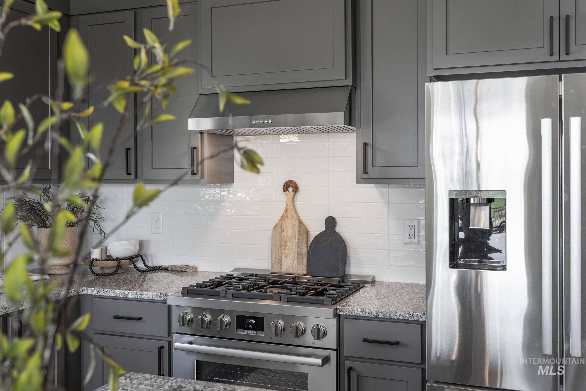 Kitchen featuring gray cabinets, stainless steel appliances, light stone counters, and decorative backsplash
