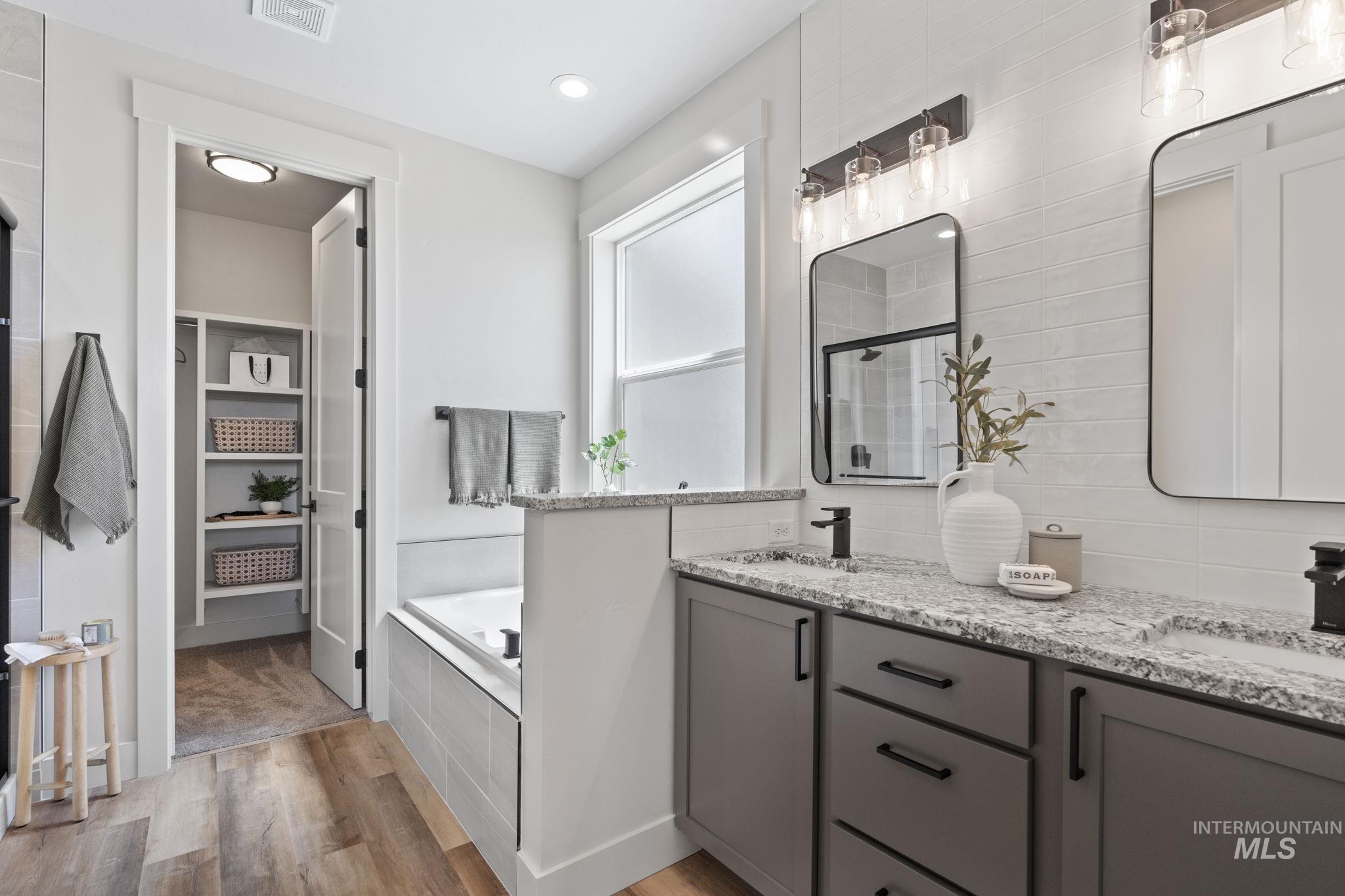 Full bathroom featuring a shower stall, a garden tub, light wood finished floors, double vanity, and recessed lighting