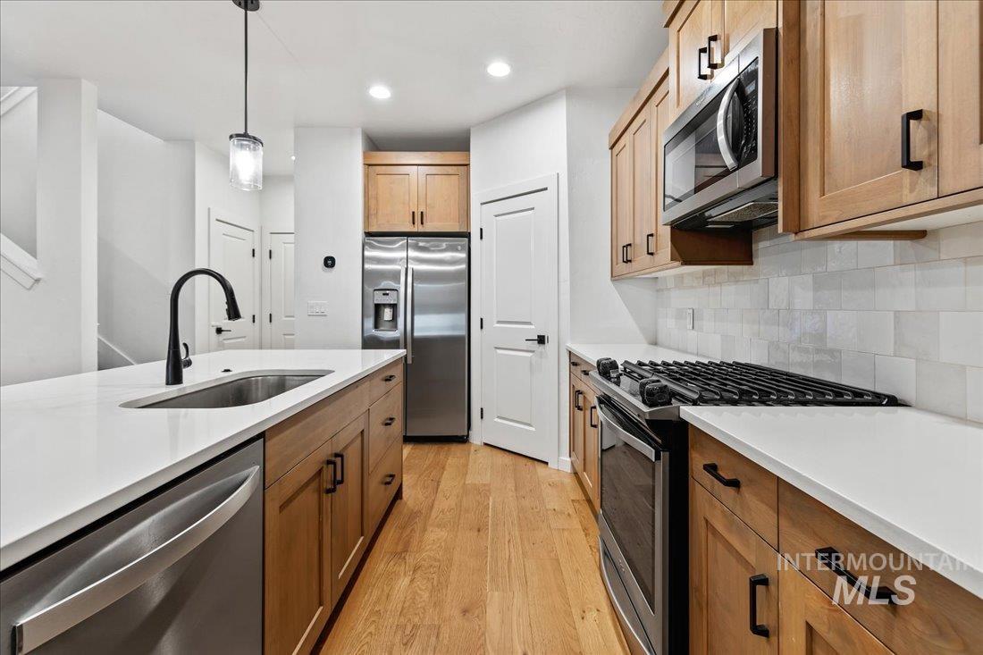Kitchen featuring stainless steel appliances, light wood-type flooring, decorative light fixtures, decorative backsplash, and recessed lighting