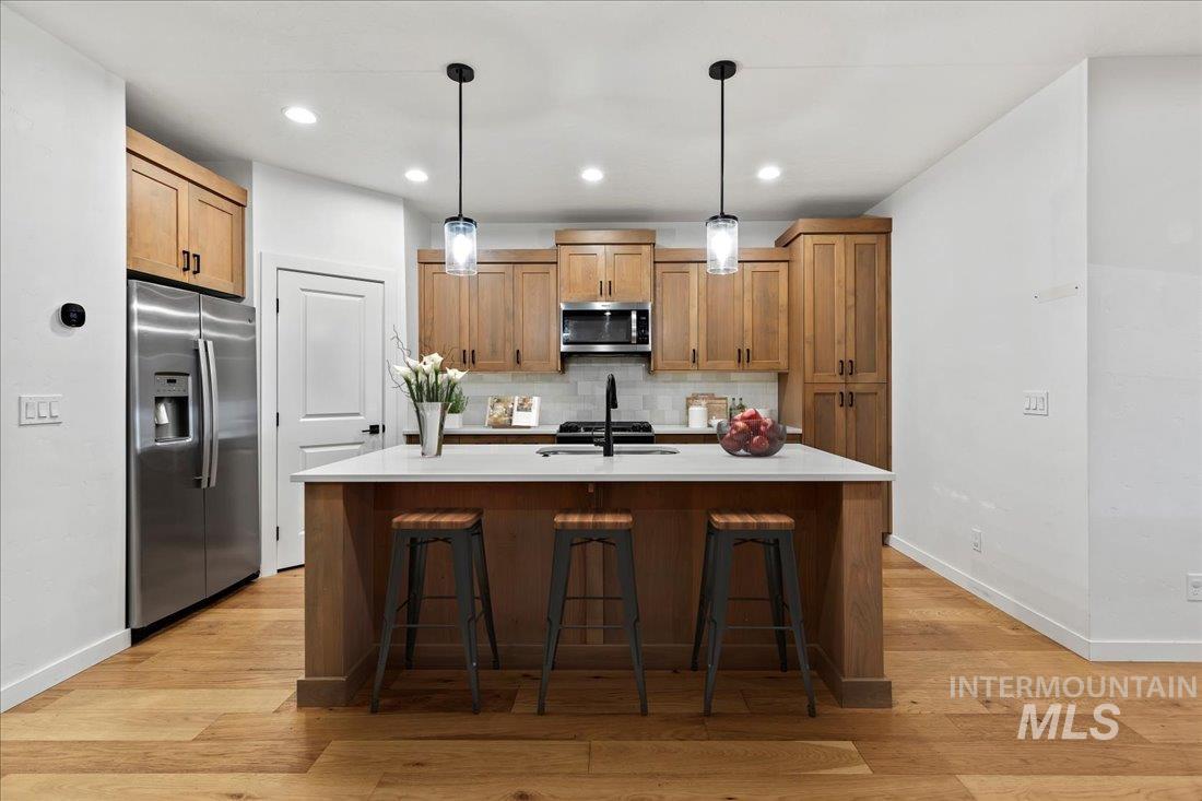 Kitchen featuring pendant lighting, stainless steel appliances, a breakfast bar area, tasteful backsplash, and a kitchen island with sink